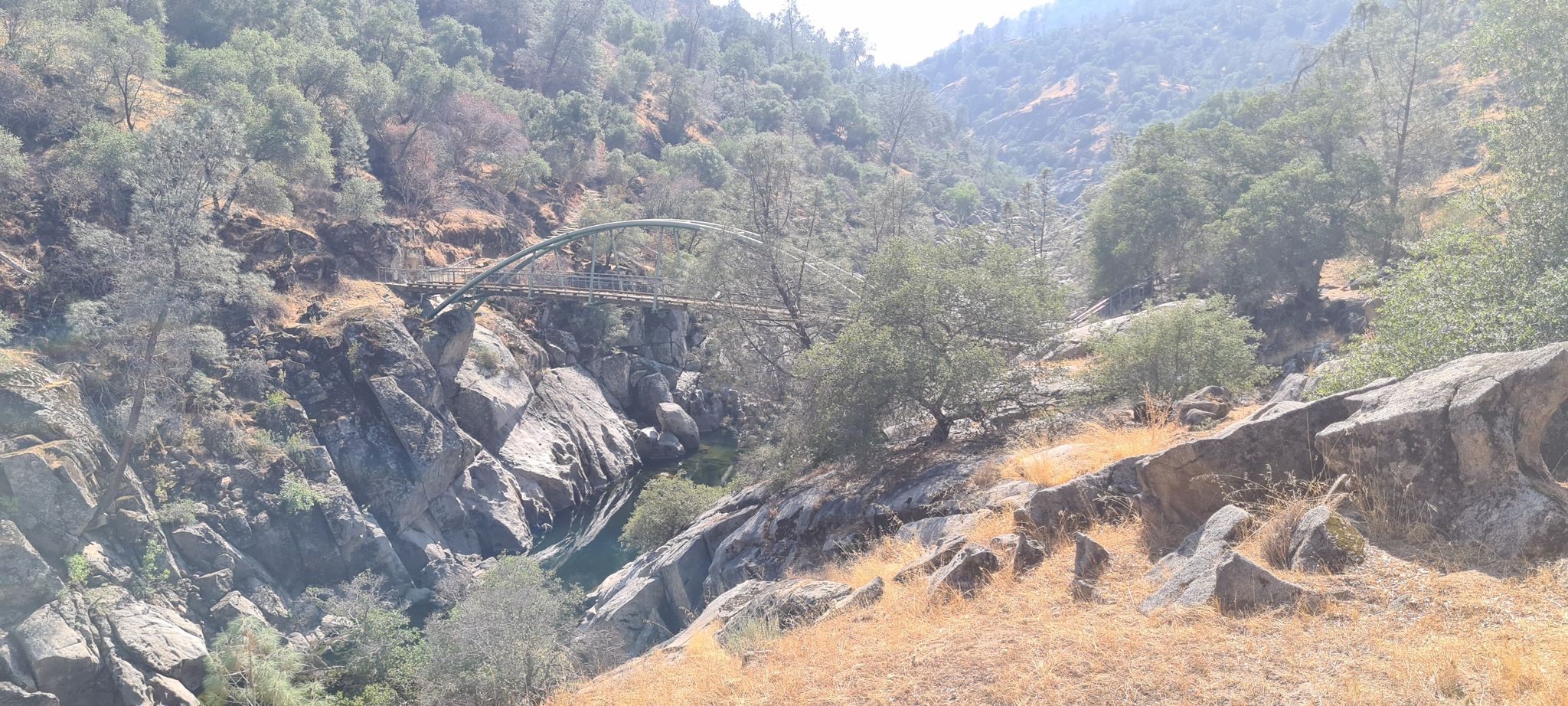 Arched bridge spans a rocky canyon with a river under bright daylight. - Pa'san Ridge Trail