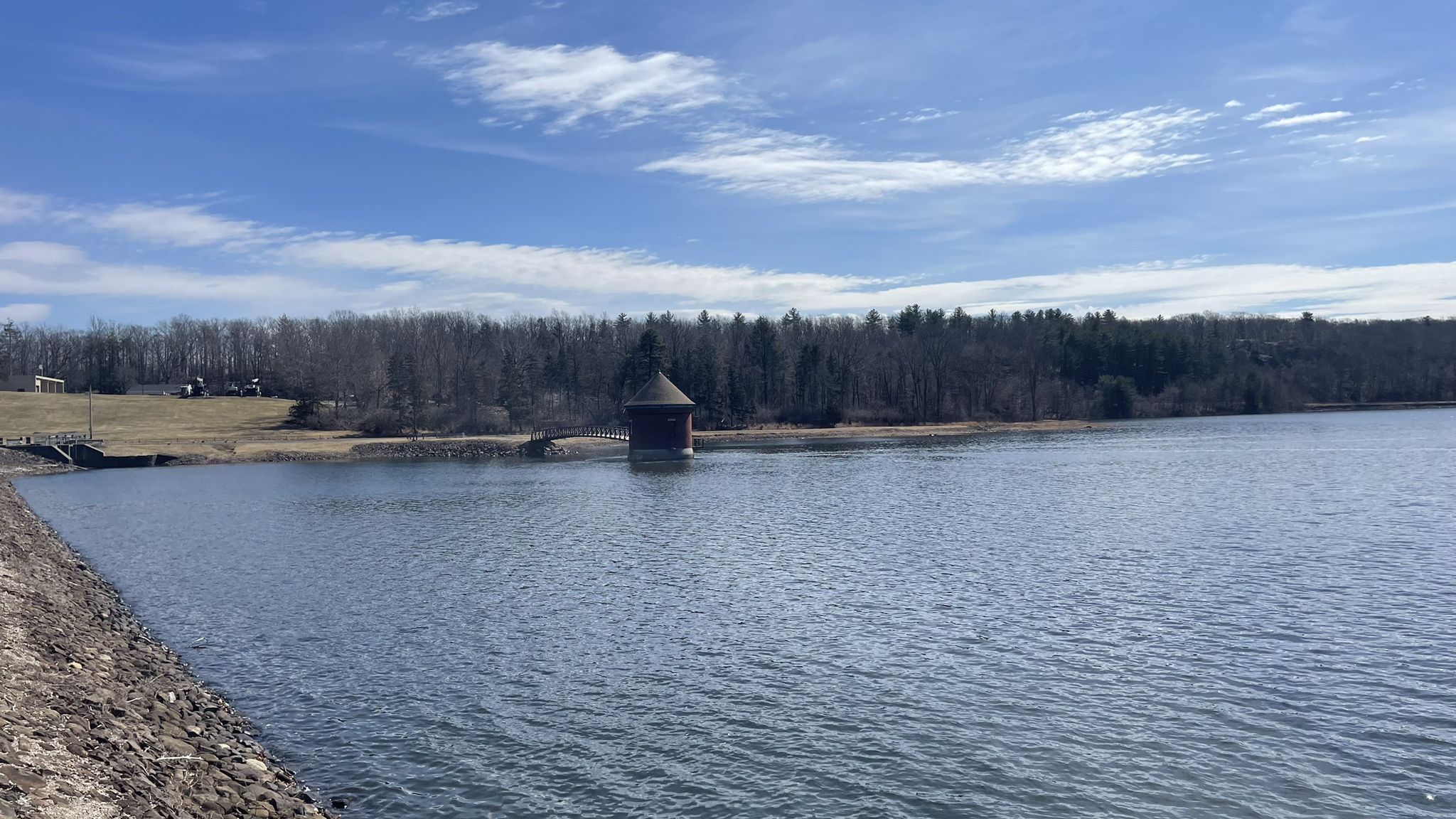 A wide lake with a small building, surrounded by distant bare trees under a bright sky. - Farmington Canal Trail and Meriden Loop