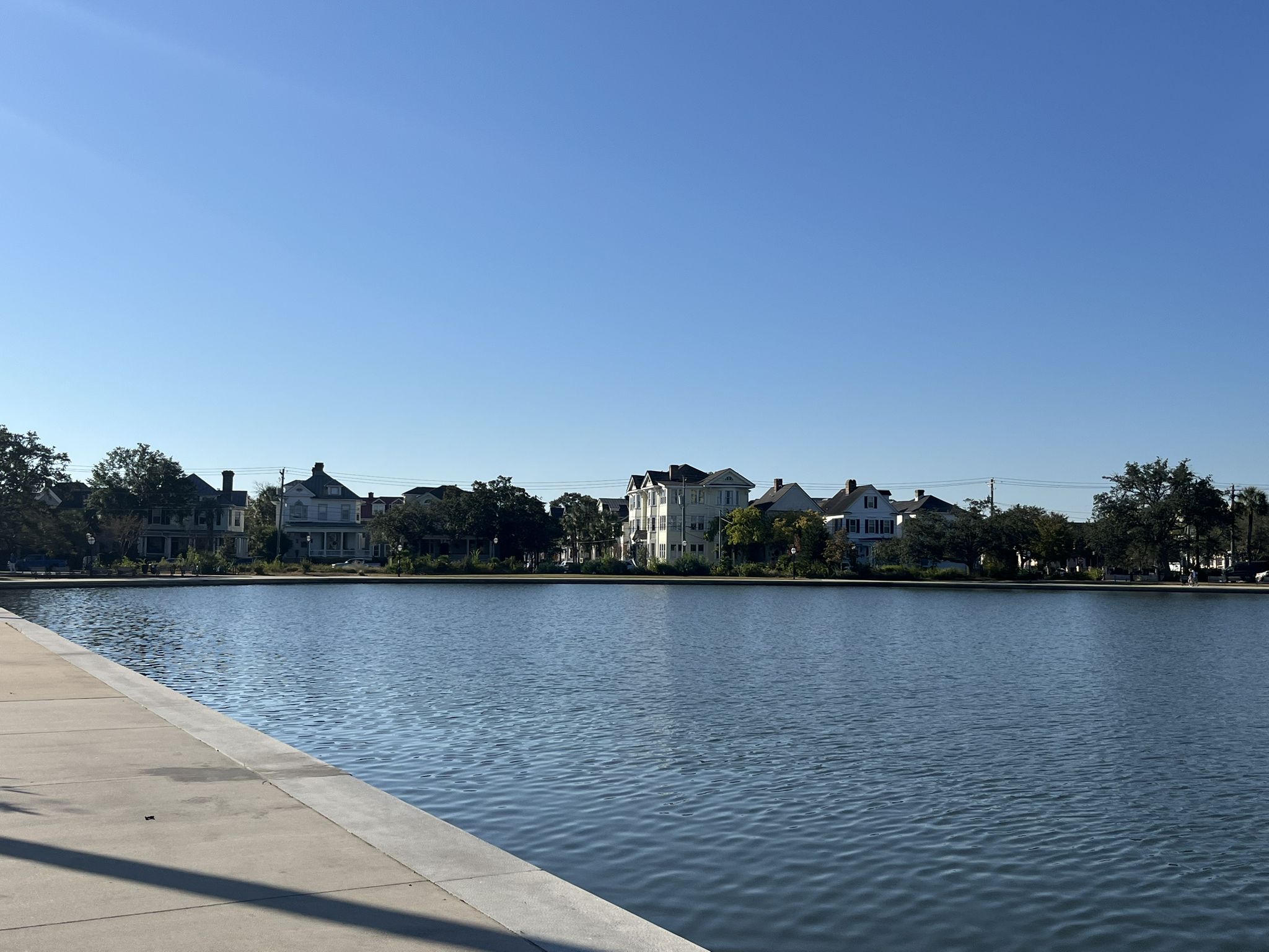 Calm water reflecting a clear sky, with houses on the distant shore. - Colonial Lake Park Loop
