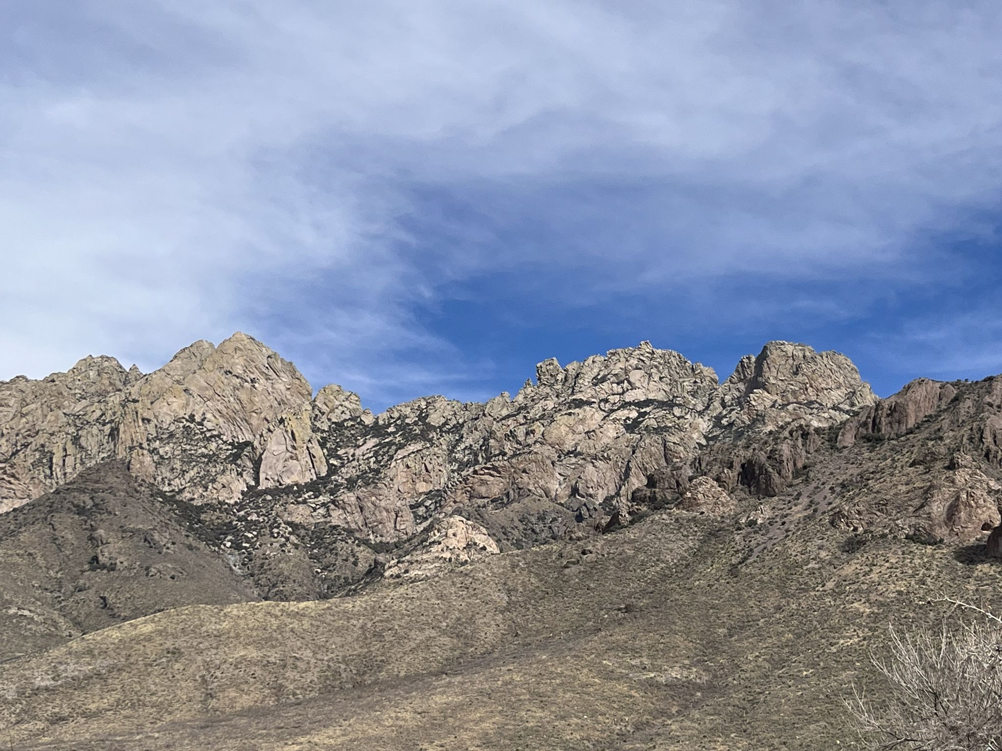 Rugged mountain range with rocky peaks and dry vegetation under a partly cloudy sky. - La Cueva Loop Trail
