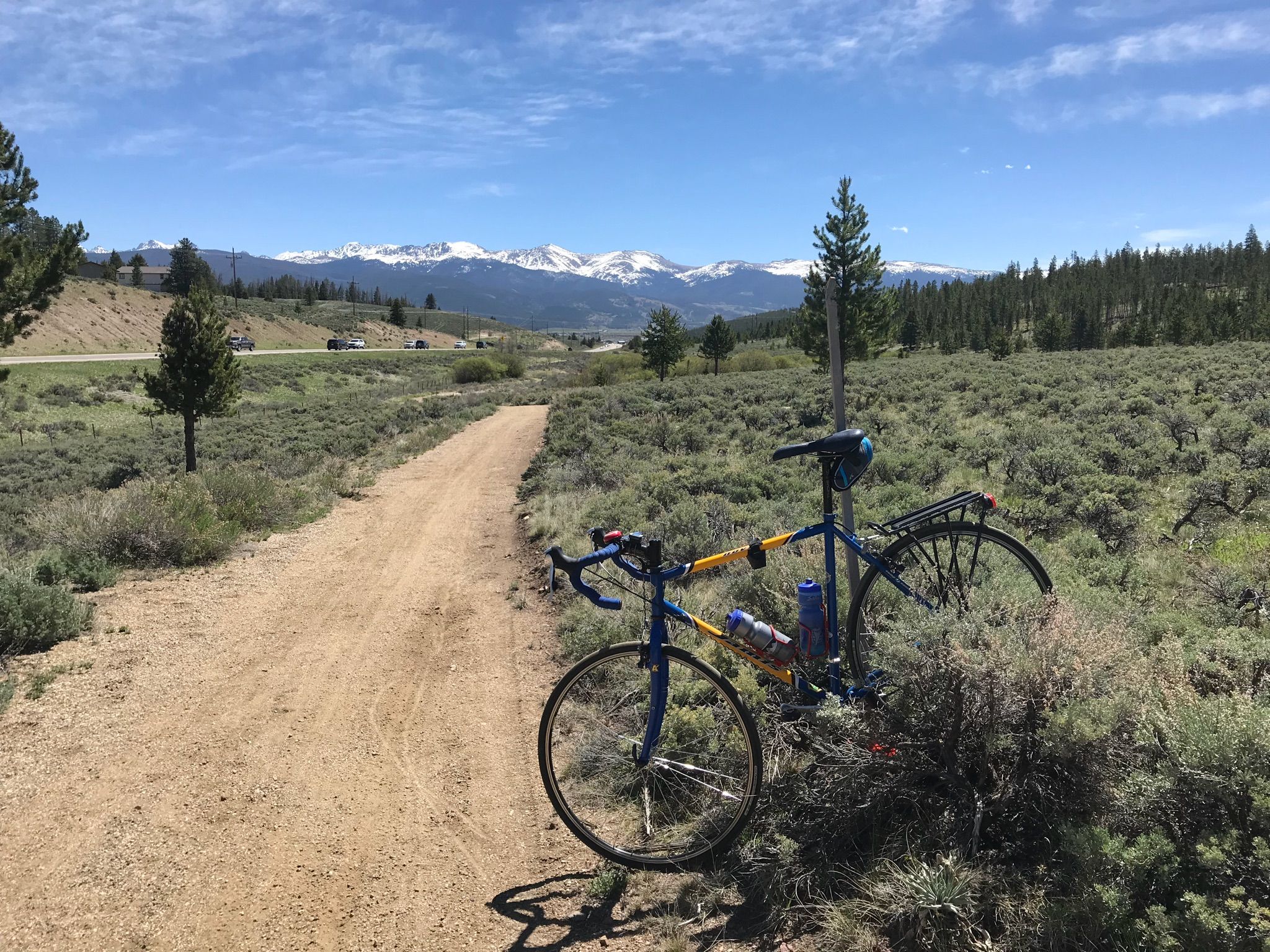 A bicycle resting beside a dirt path, with distant snowy mountains and trees. - Fraser – Fraser River Trail loop from Snow Mountain Ranch - YMCA - Northbound