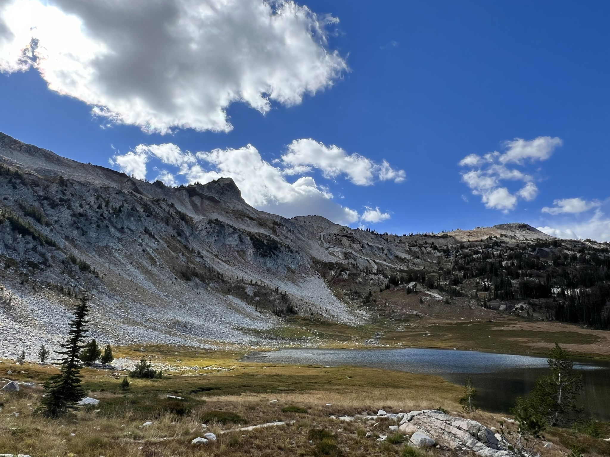 Small lake at the base of a rocky mountain under a bright, cloudy sky. - Epic Mirror Lake campsite – Upper Lake loop from Moccasin Lake
