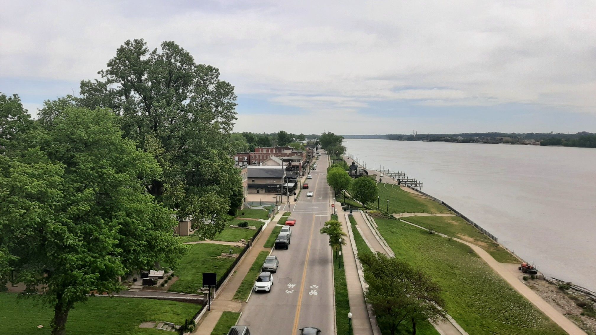 Overhead view of a road alongside a wide river, with trees and buildings. - Big 4 Walking Bridge