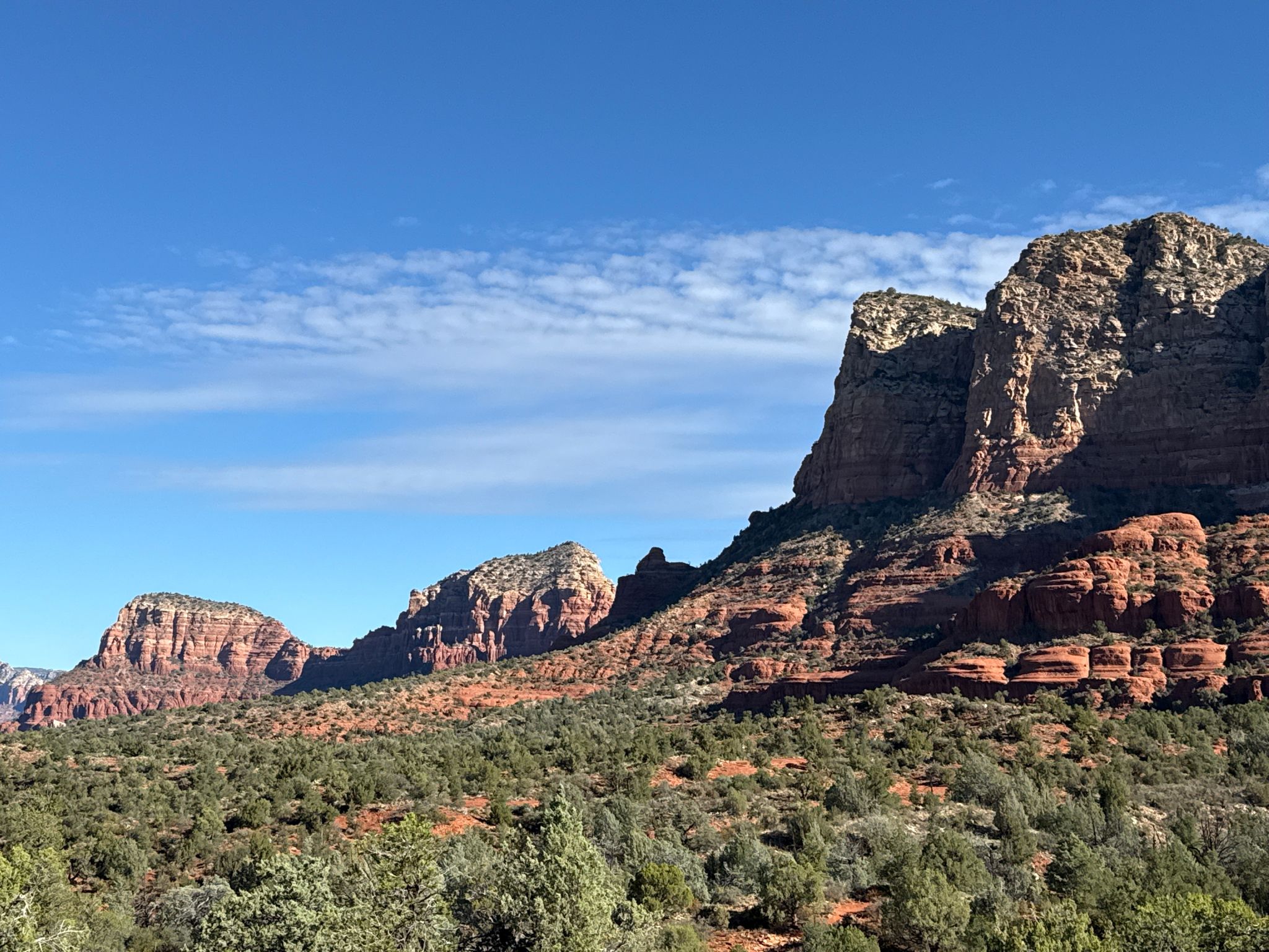 Panoramic view of layered red rock mountains and green trees under a blue sky. - Courthouse Butte and Bell Rock Loop