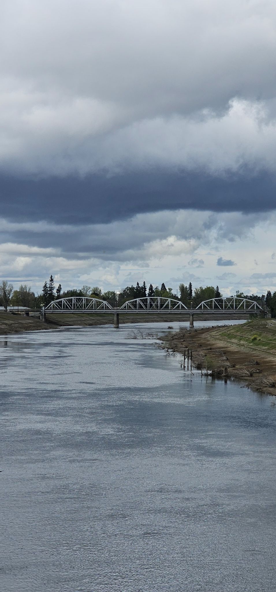 White truss bridge spans a wide river under a dramatic, cloudy sky. - American River Bike Trail