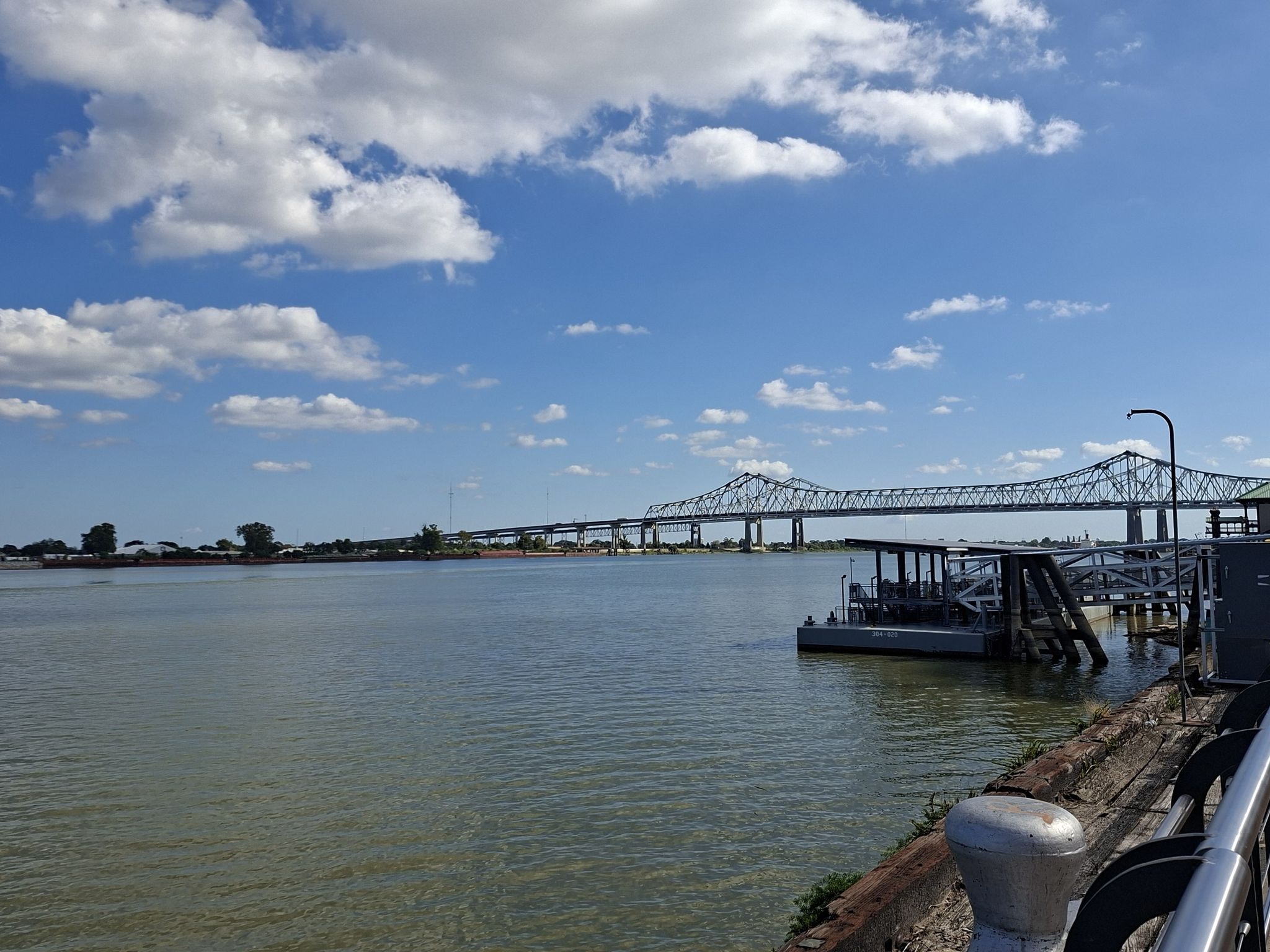 Expansive river with a long bridge in the distance under a cloudy sky. - Woldenberg Riverfront Park – Audubon Aquarium loop from New Orleans