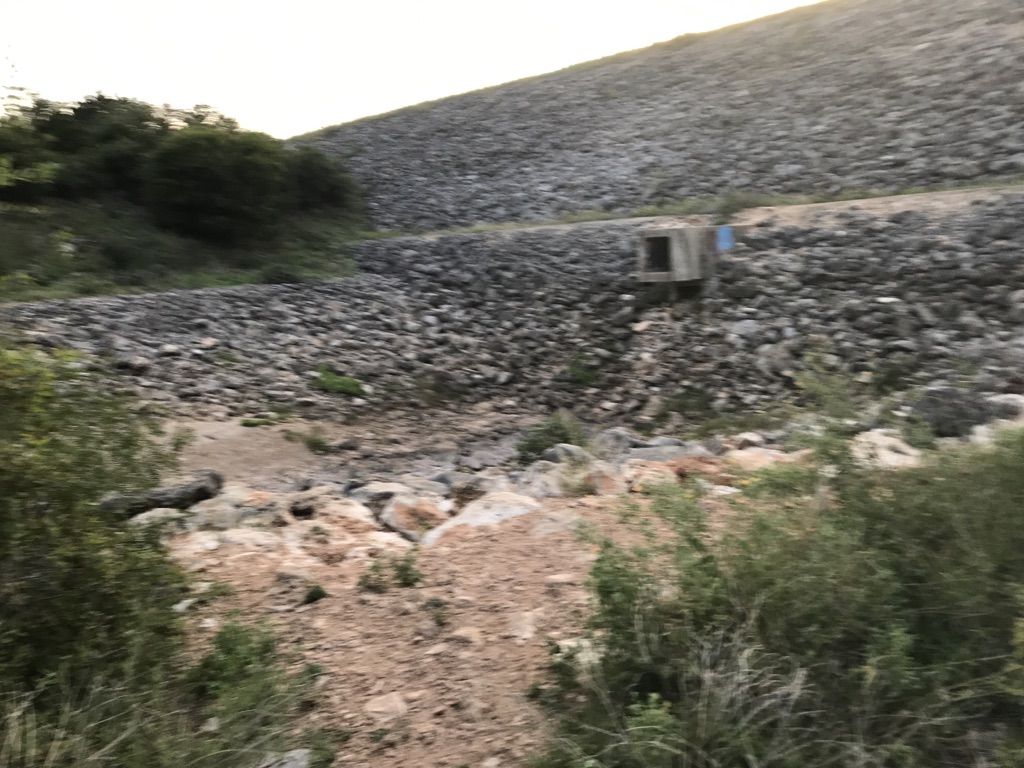 Rocky slope with a concrete culvert, dry creek bed, and sparse green bushes. - Dante's Trail Loop