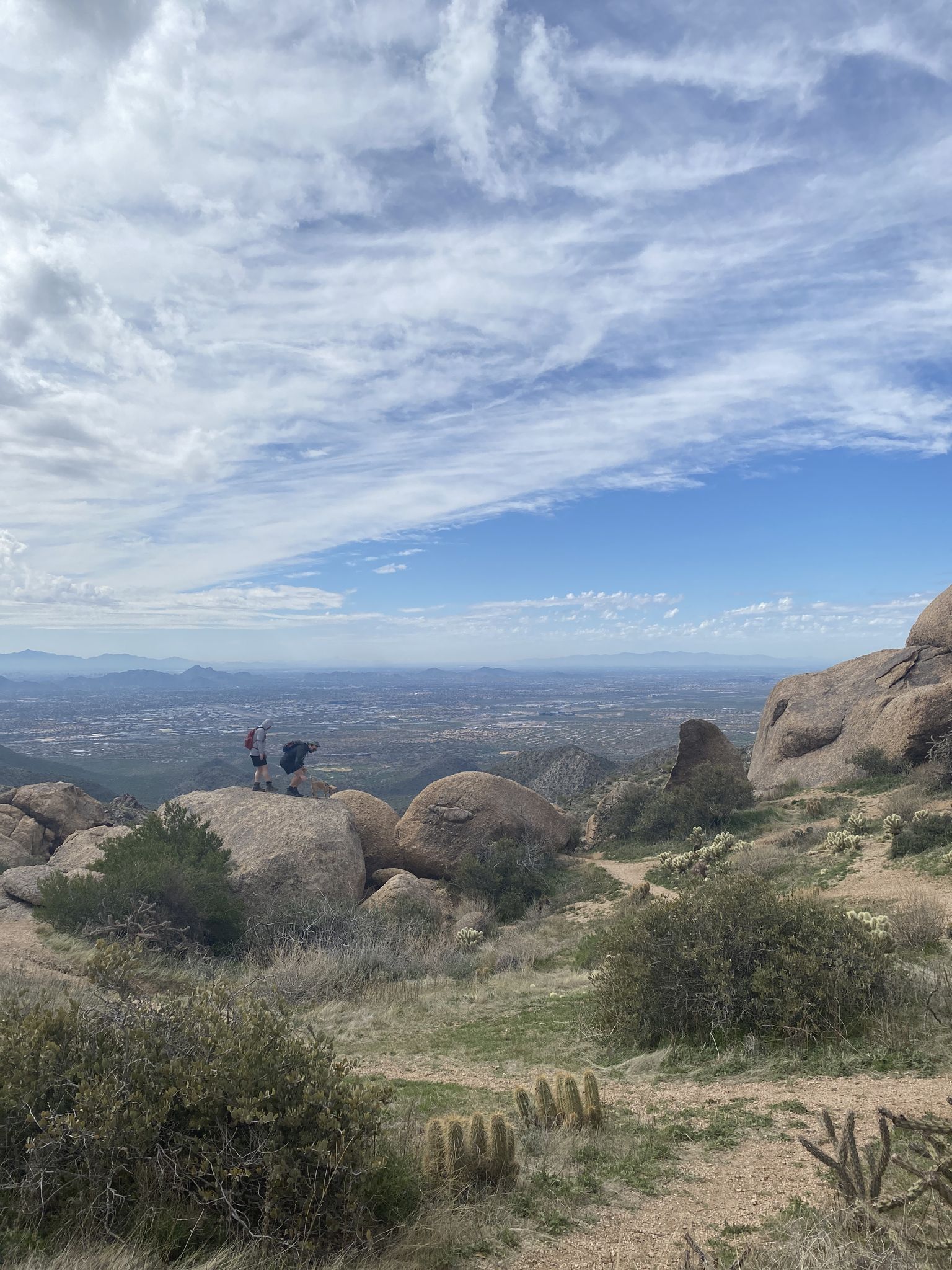 Two hikers stand on rocks, enjoying a vast, cloudy desert landscape view. - Tom's Thumb Trail