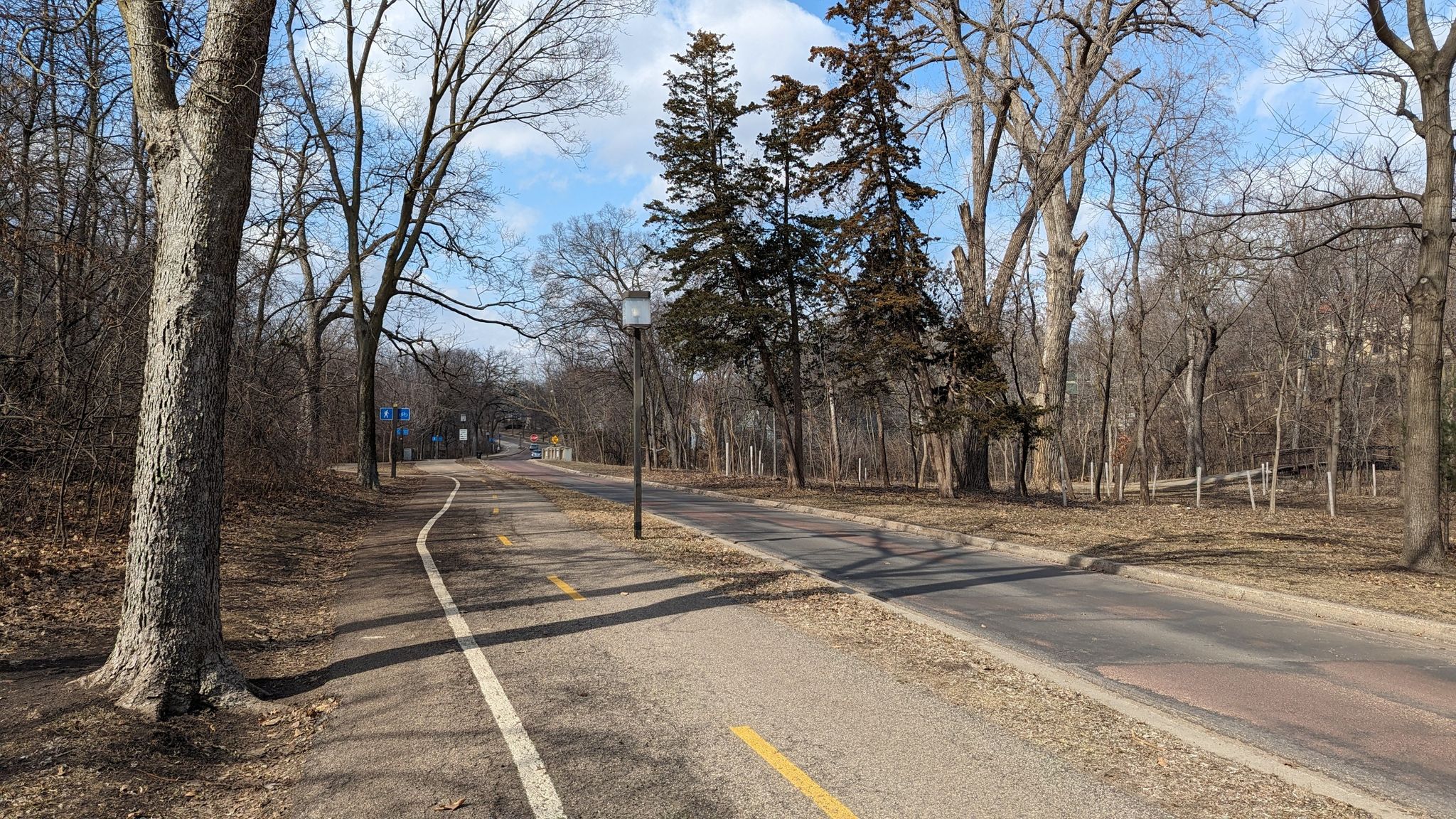 A paved path and road wind through a park with bare trees. - Minnehaha Creek Park – Lake Harriet South Beach loop from Southwest