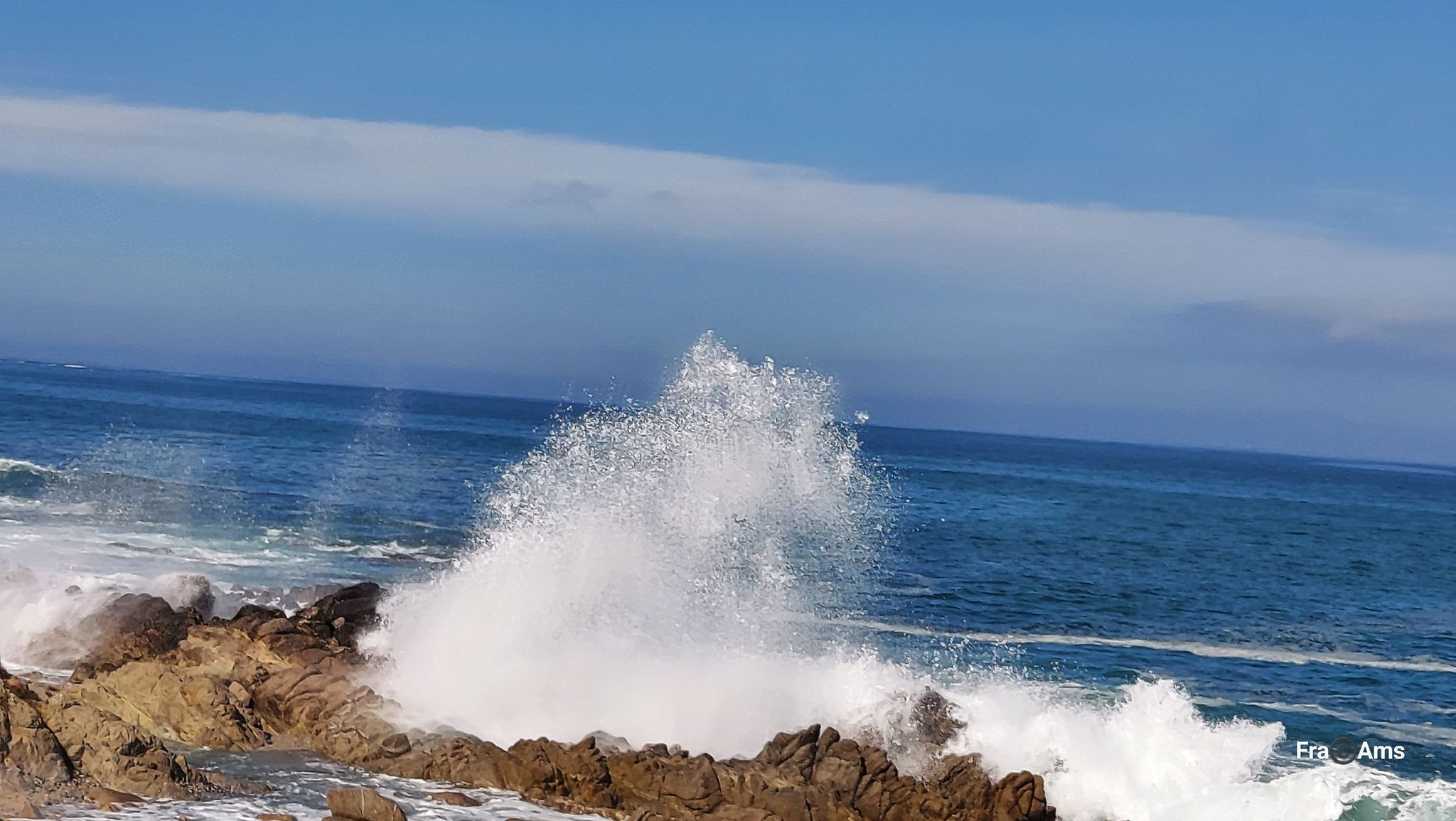 Large ocean wave crashing dramatically against coastal rocks under a blue sky. - Shoreline Park Path – Cannery Row loop from Monterey