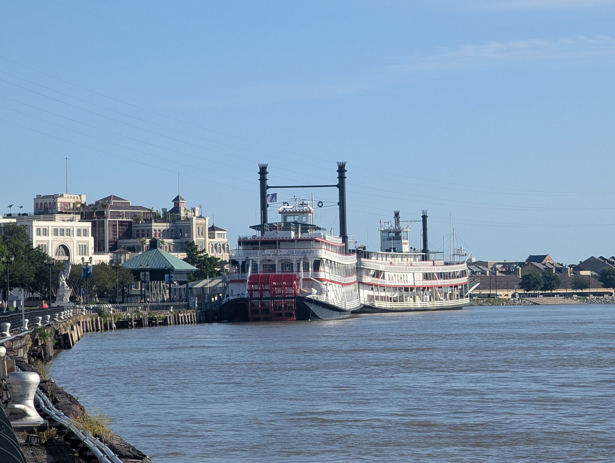 Two paddlewheel boats docked along a river with historic city buildings. - Woldenberg Riverfront Park – Moon Walk loop from New Orleans