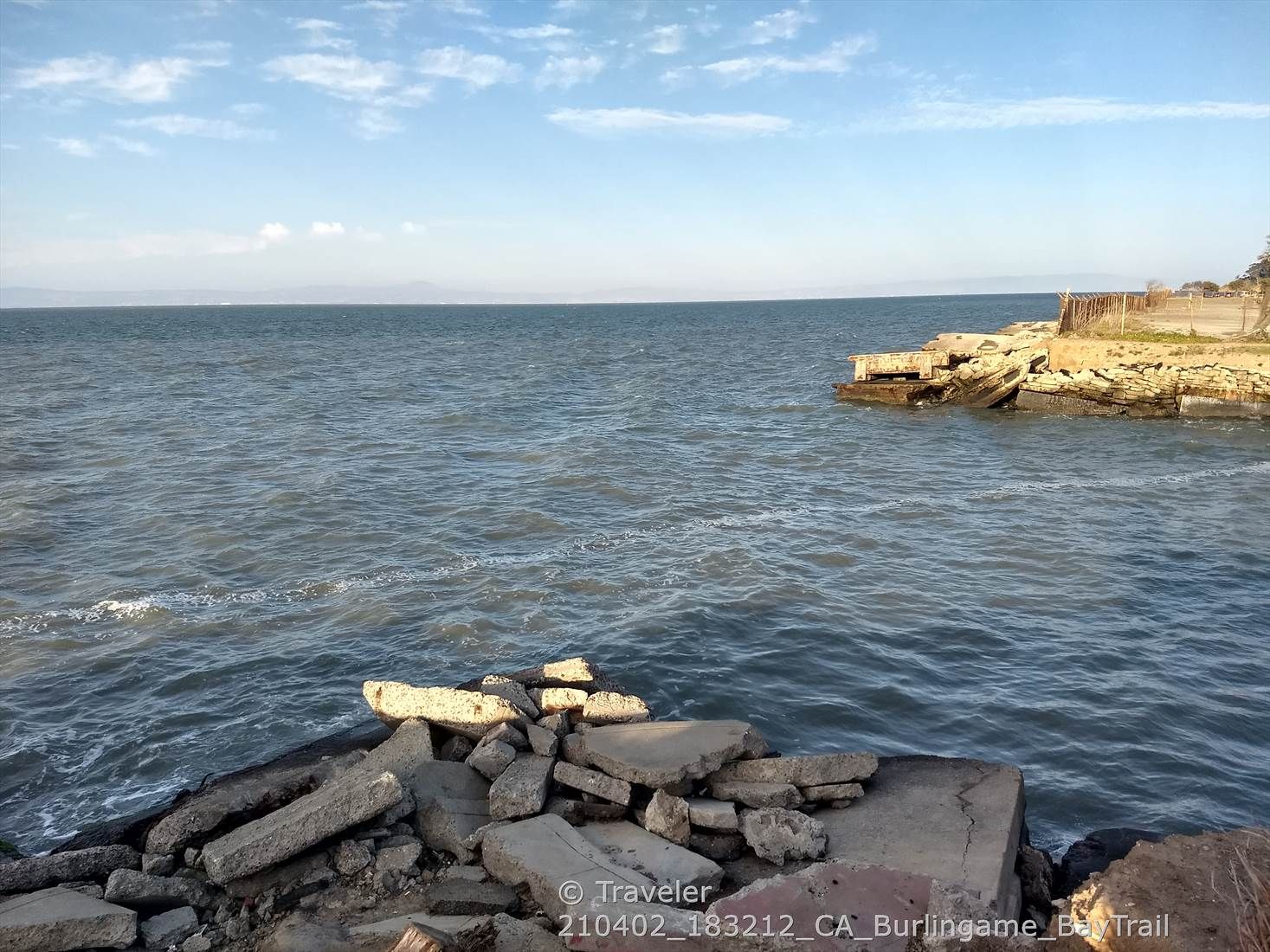 Choppy water with rocky debris in foreground and distant land under a bright sky. - San Francisco Bay Trail: Bayside Park Loop