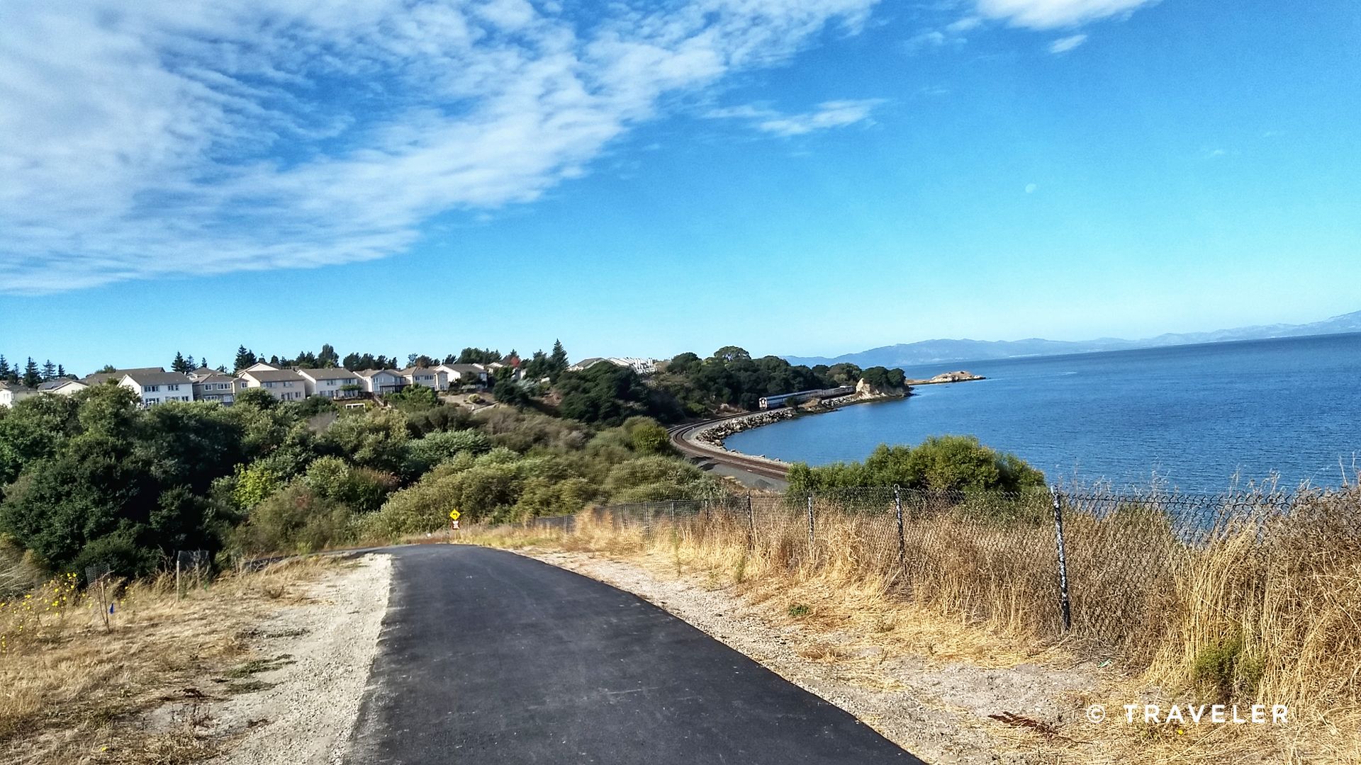 Paved path overlooking a sunny coastline with houses and calm blue water. - Pinole Shores Park – Lone Tree Point Regional Park loop from Pinole