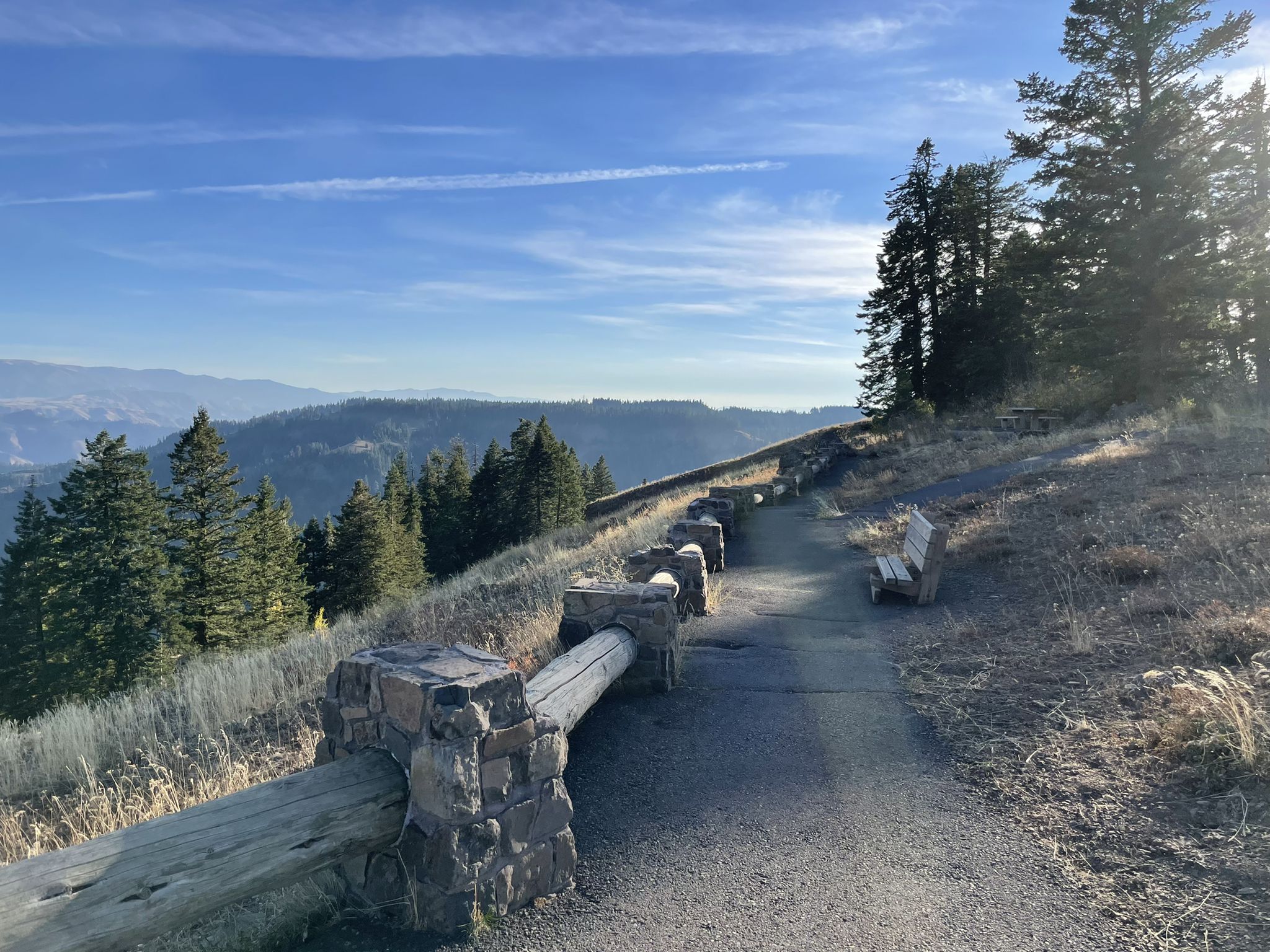 Paved path with wooden fence and bench overlooking sunny, forested mountains. - Hells Canyon via Indian Crossing Campground loop