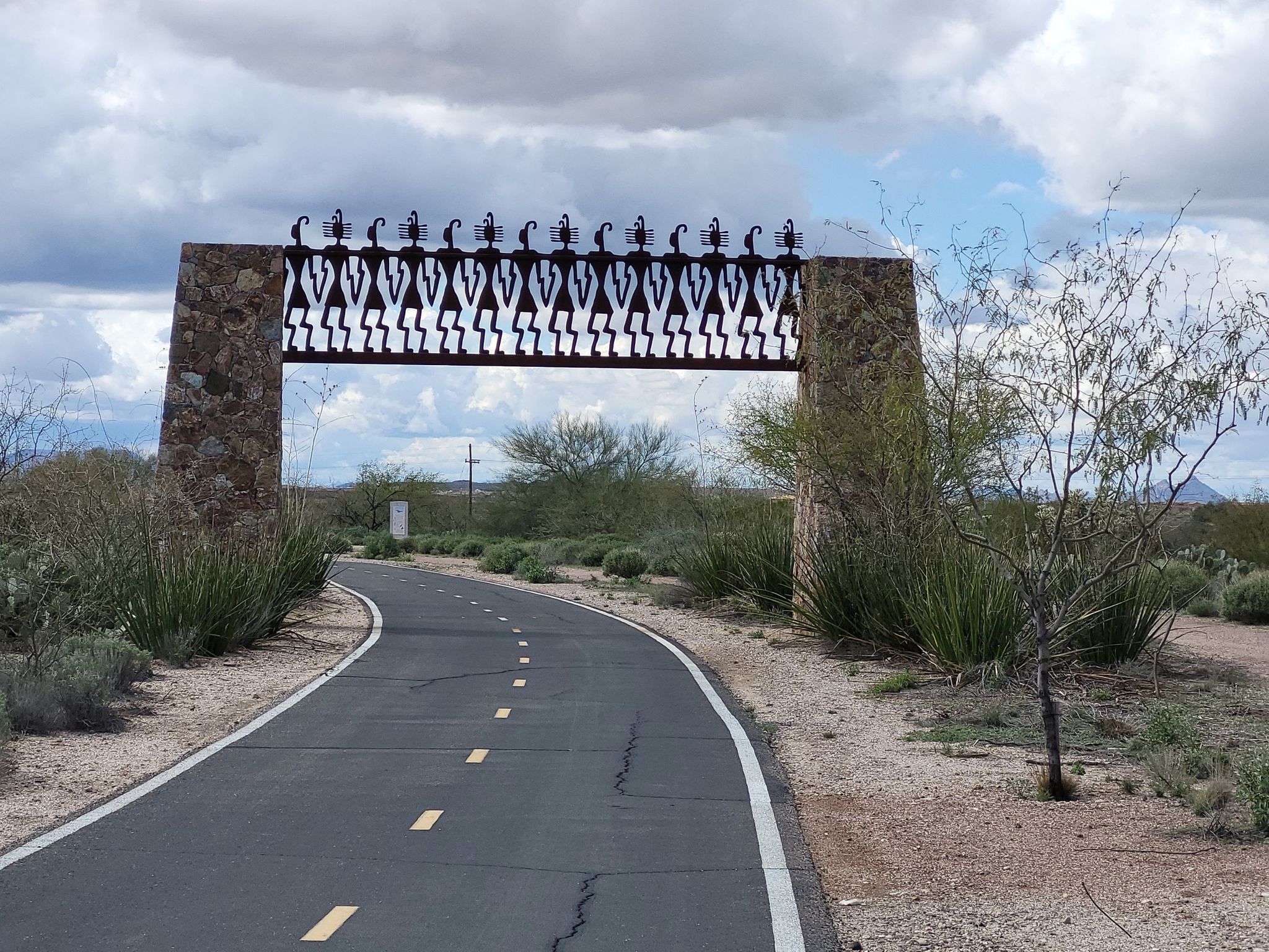 Paved path curving under a decorative metal archway in desert landscape. - Joining Hands loop from Esmond Station