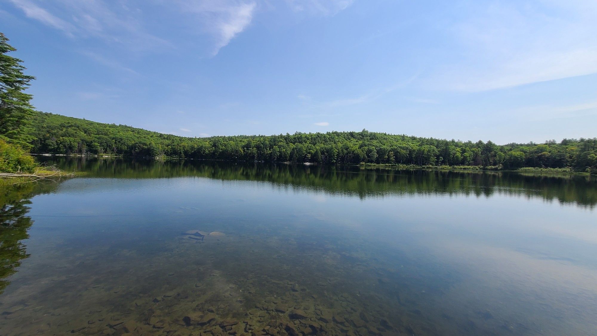Calm lake reflects blue sky and green forested hills on a sunny day. - Bald Hill – Quarry Hill loop from White River Junction