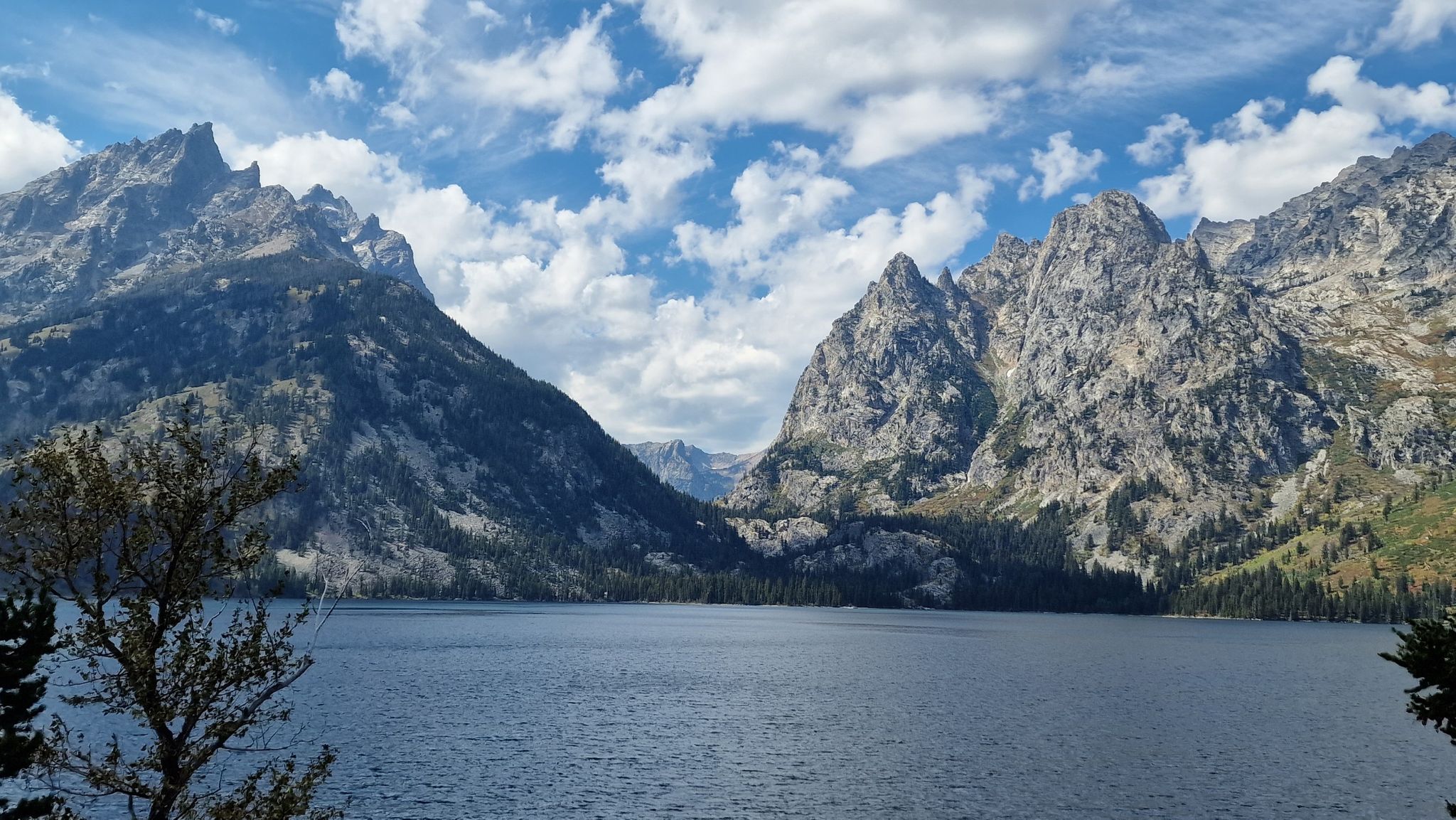 Serene lake framed by towering, rocky mountains under a blue sky. - Jenny Lake Overlook – Jenny Lake loop from Teton