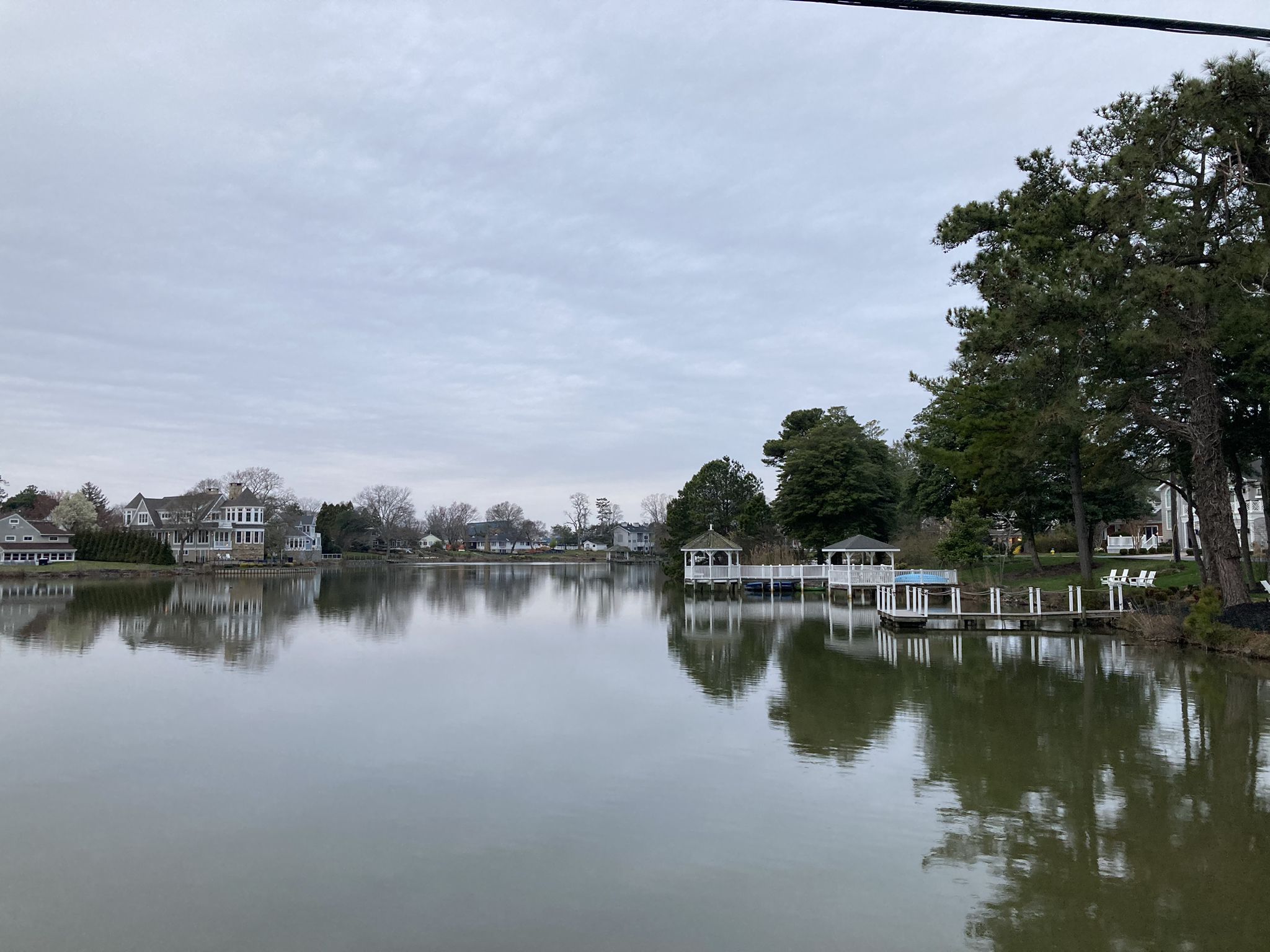A calm lake reflecting houses and docks, surrounded by trees under a cloudy sky. - Delaware Bicycle Route 1