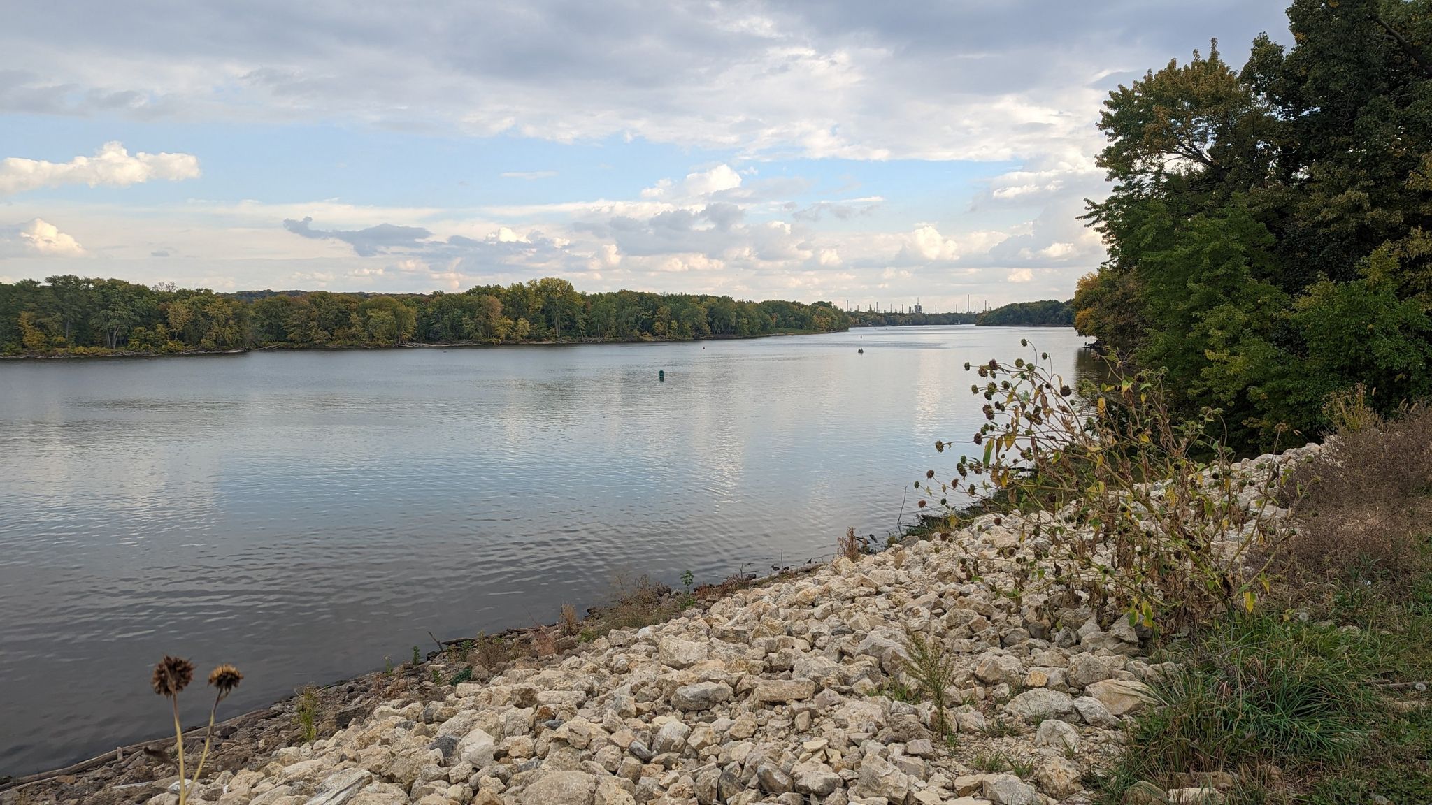 Wide river with forested banks under a cloudy sky, rocky foreground. - Mississippi River Greenway Loop