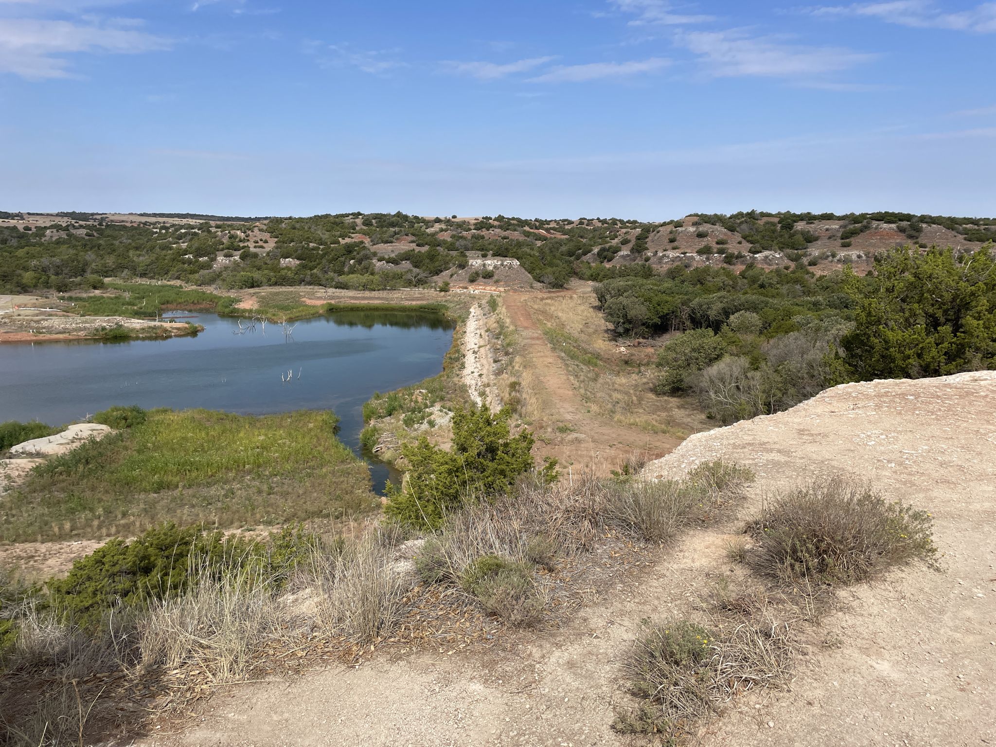 Bright daylight illuminates a lake beside a dirt path in a dry, hilly landscape. - Inspiration Point Loop