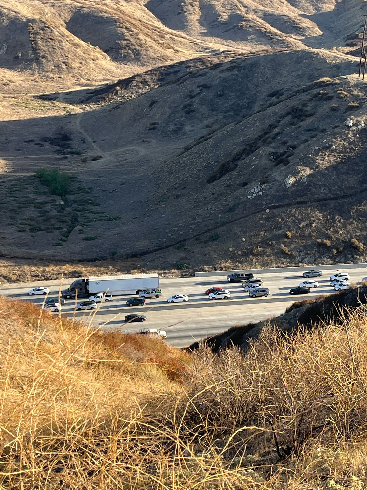 Busy highway with cars and trucks winding through dry, sunlit hills. - Caroline Park – Panorama Point loop from San Bernardino–Tippecanoe