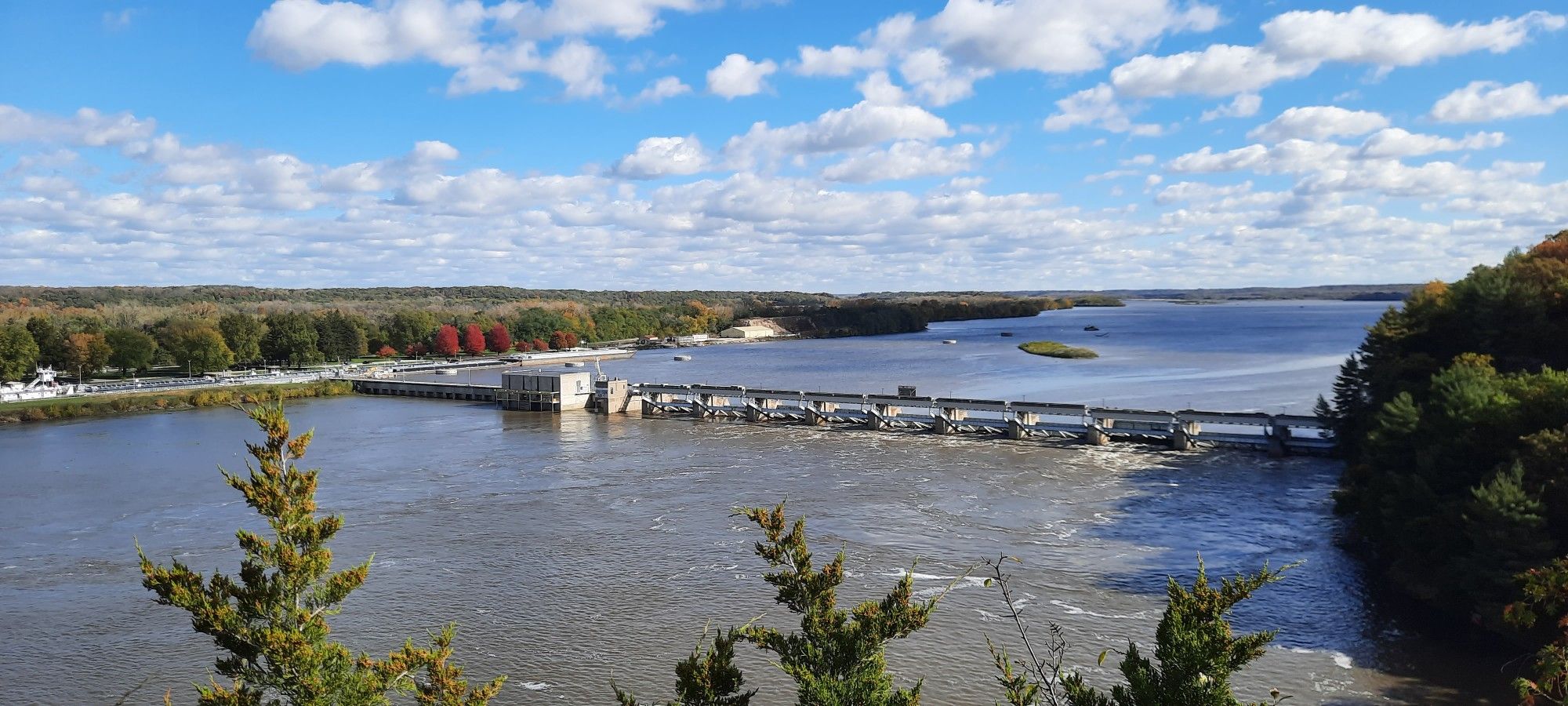 A dam spans a wide river, surrounded by colorful autumn trees under a blue sky. - Starved Rock – Wildcat Canyon East Platform loop from Starved Rock State Park Visitors Center