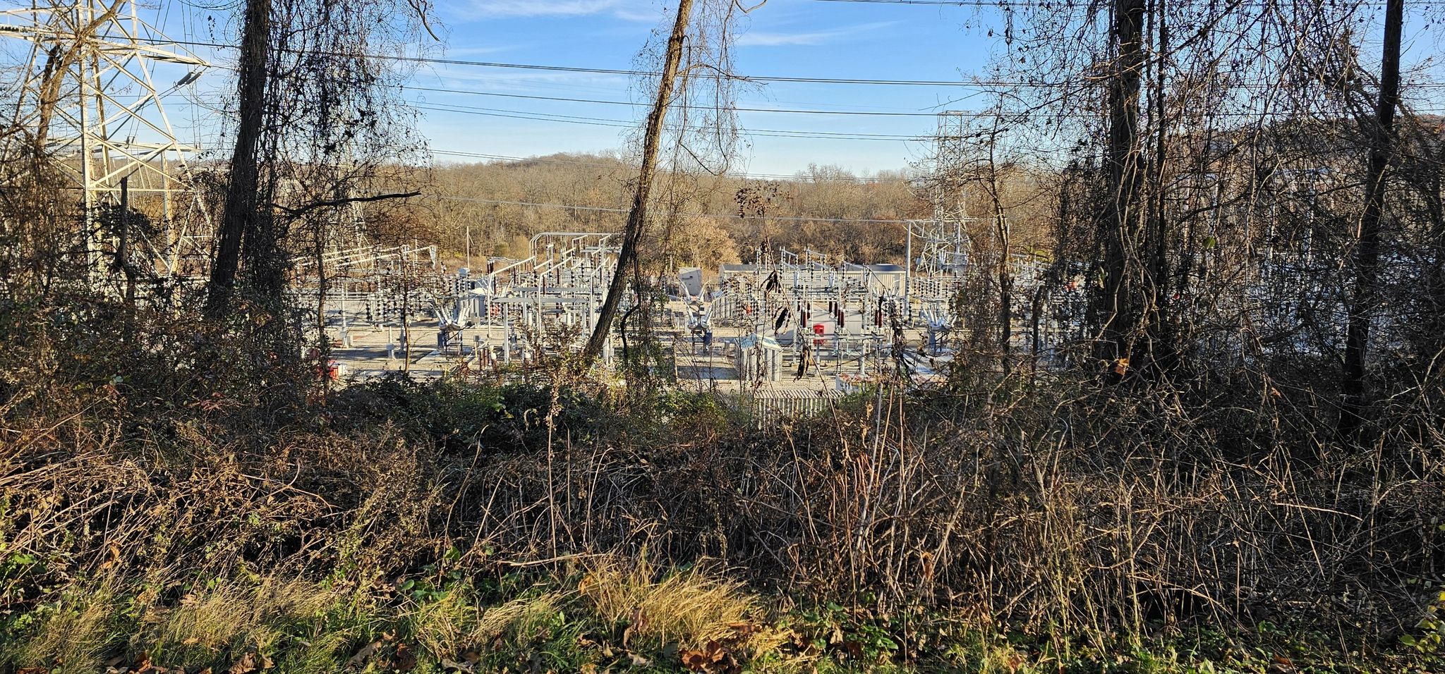 Power substation visible through bare trees and brush on a sunny day. - Van Cortlandt Greenway – Woodlands Lake loop from Hawthorne
