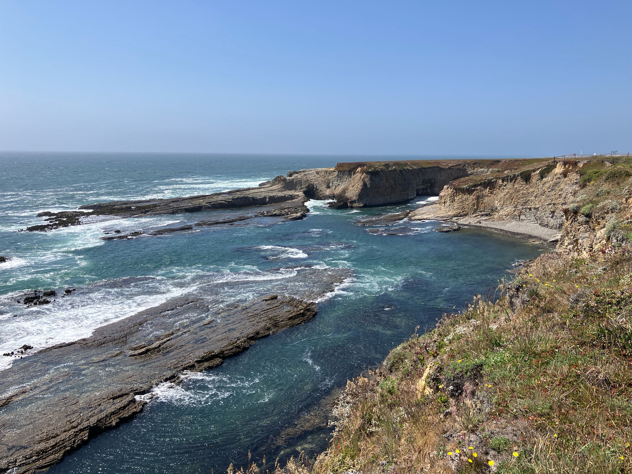 Rugged cliffs and layered rock formations meet the turquoise ocean on a sunny day. - Point Arena-Stornetta Unit of the California Coastal National Monument