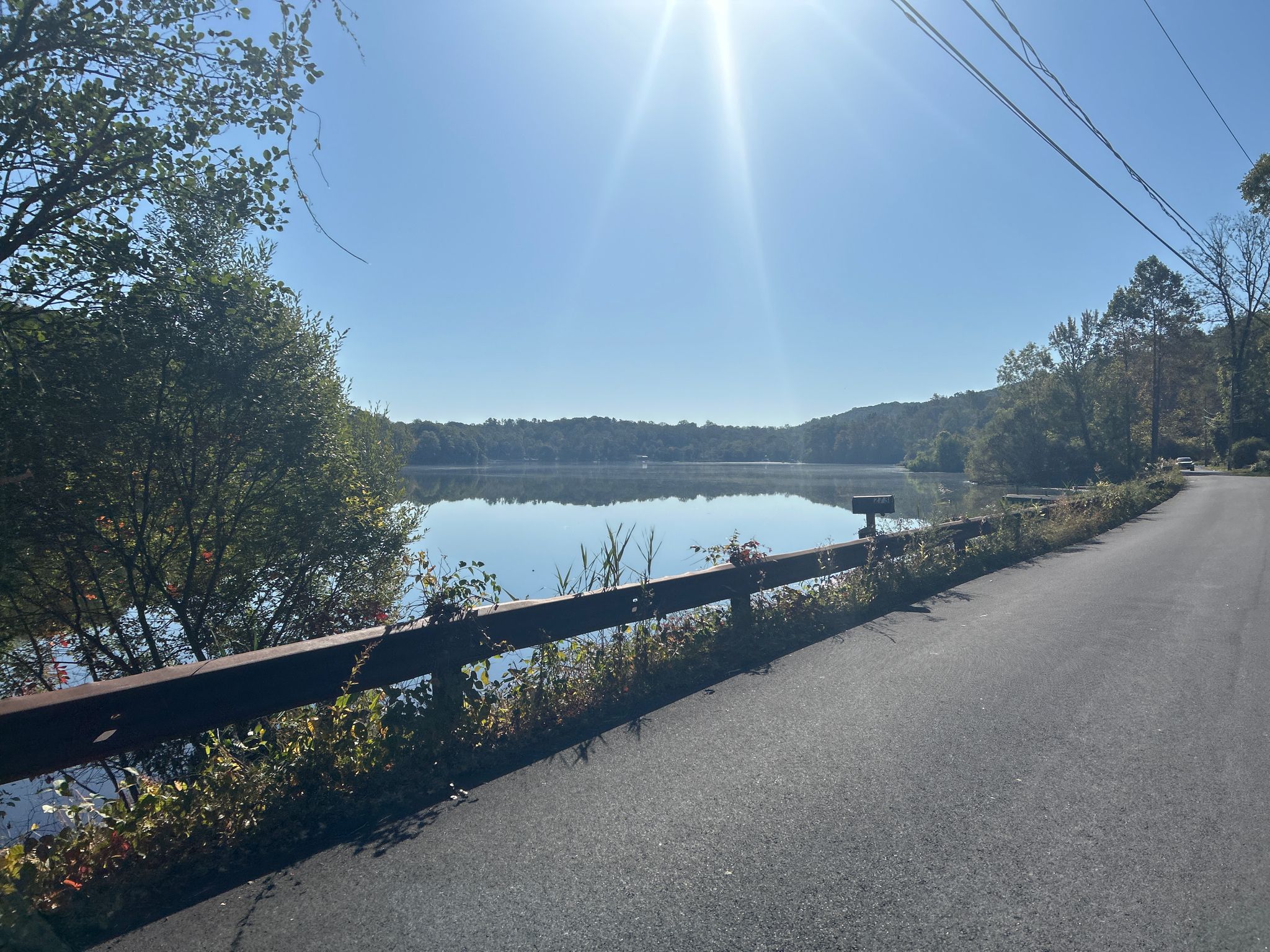 Sunny road next to a shimmering lake with bright sun glare. - Goldens Bridge Loop