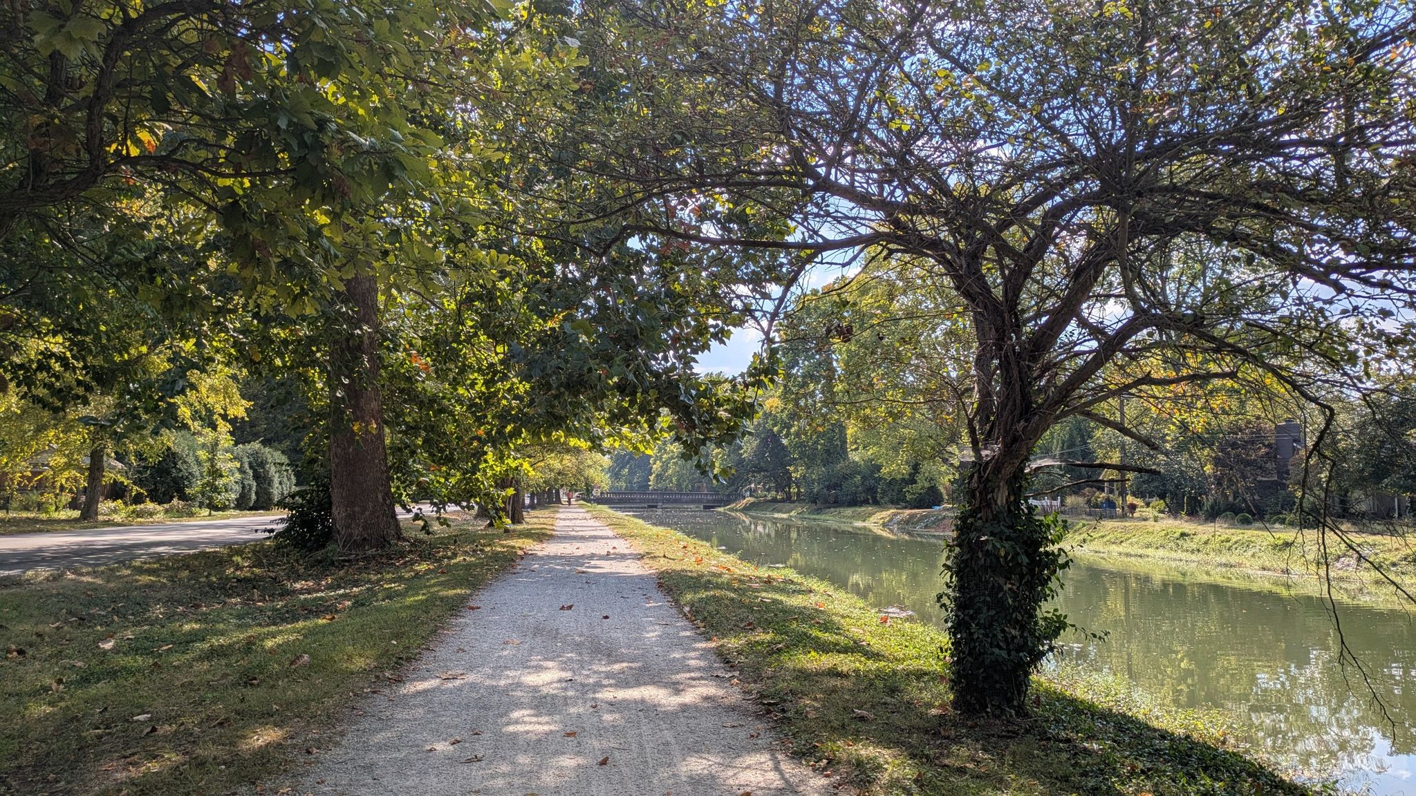 Sunny dirt path alongside a calm canal, shaded by lush green trees. - Broad Ripple Village – Broad Ripple Village loop from Indianapolis Hebrew Congregation
