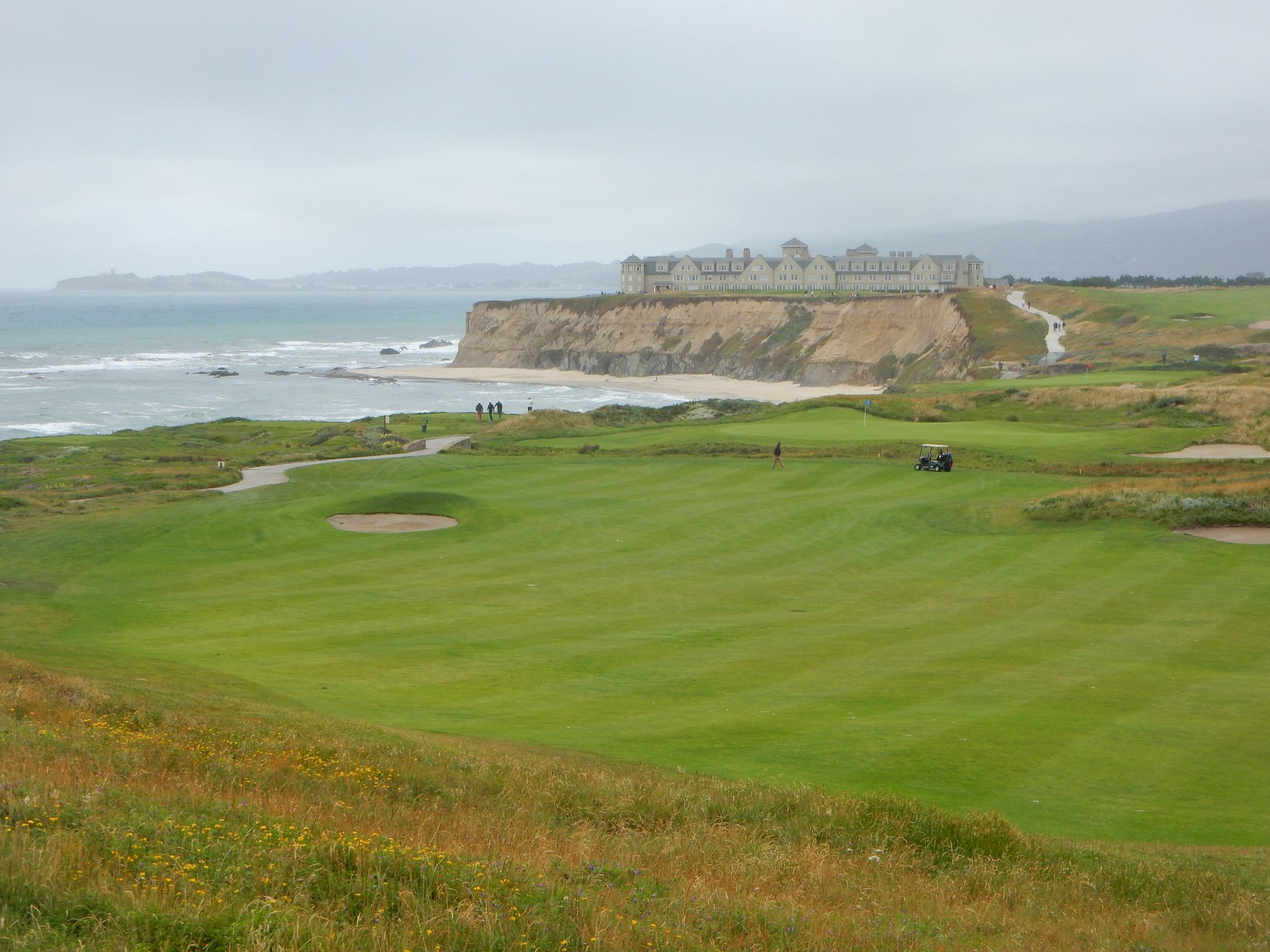 Golf course by ocean cliffs with a large building under a cloudy sky. - Half Moon Bay Coastal Trail