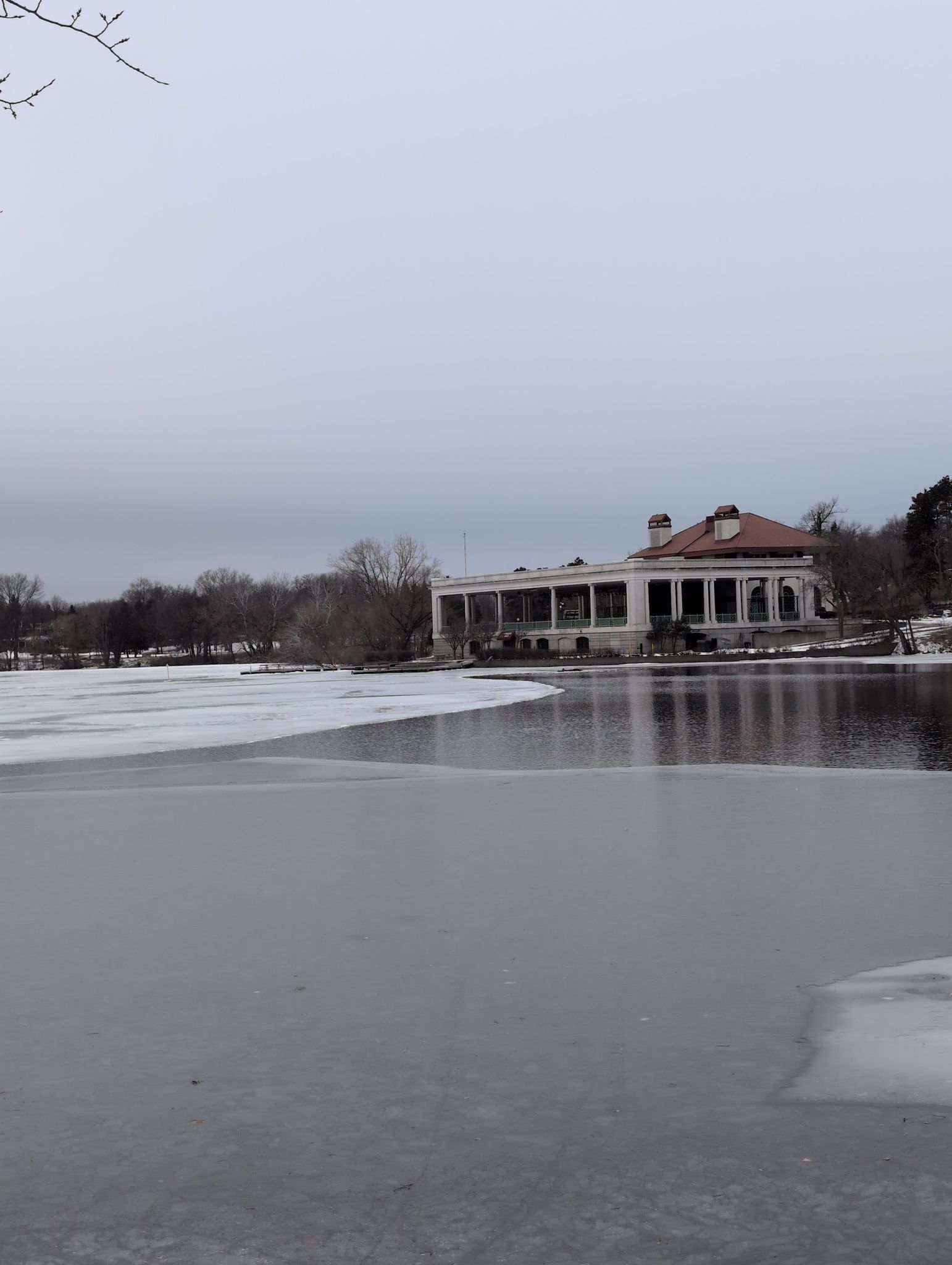 A grand building with columns overlooks a partially frozen lake on an overcast day. - Lake Phalen – Como Lake loop from Gem Lake