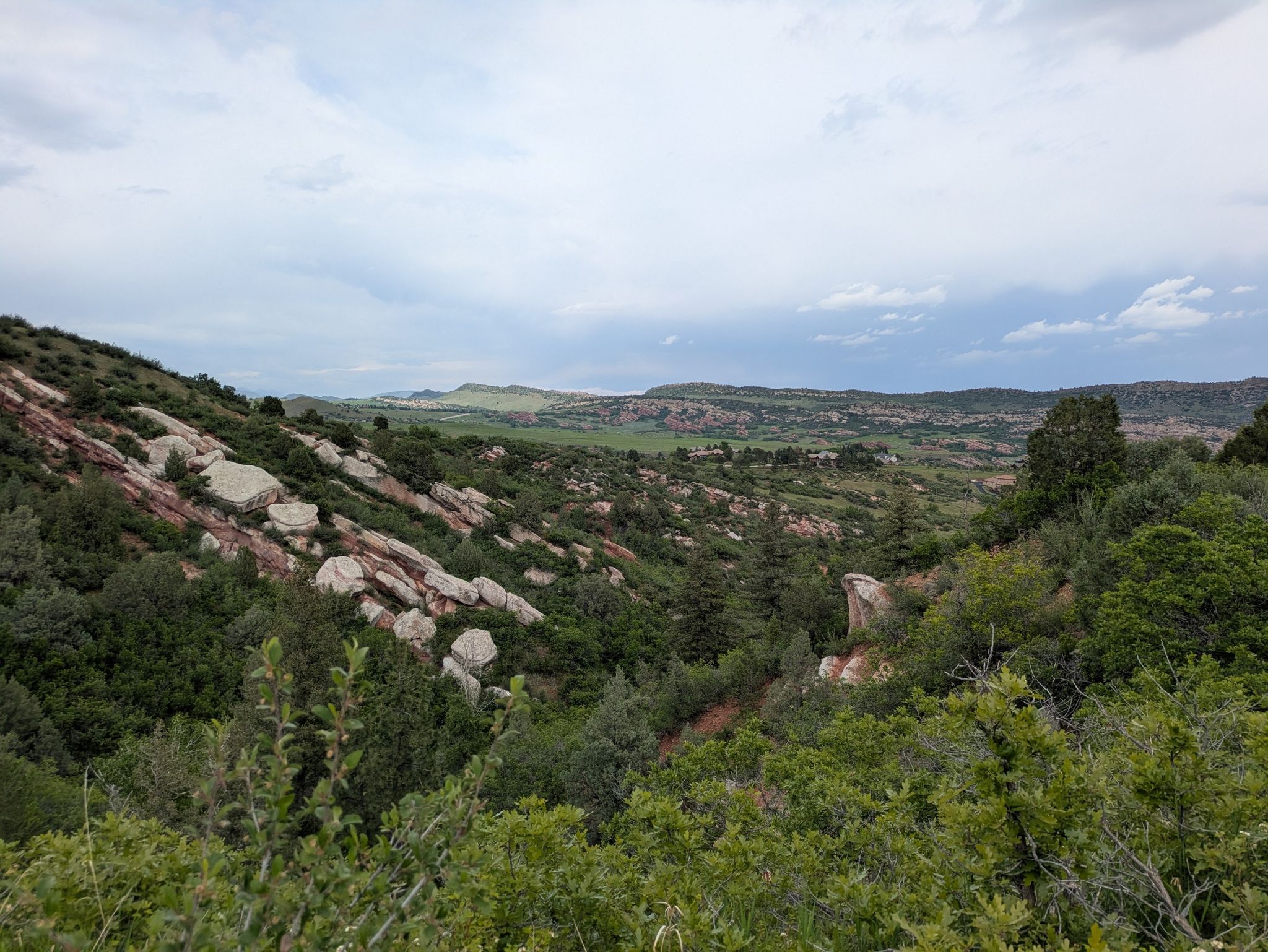Overcast view of a green valley with rocky slopes and distant fields. - Plymouth Creek to Red Mesa Loop