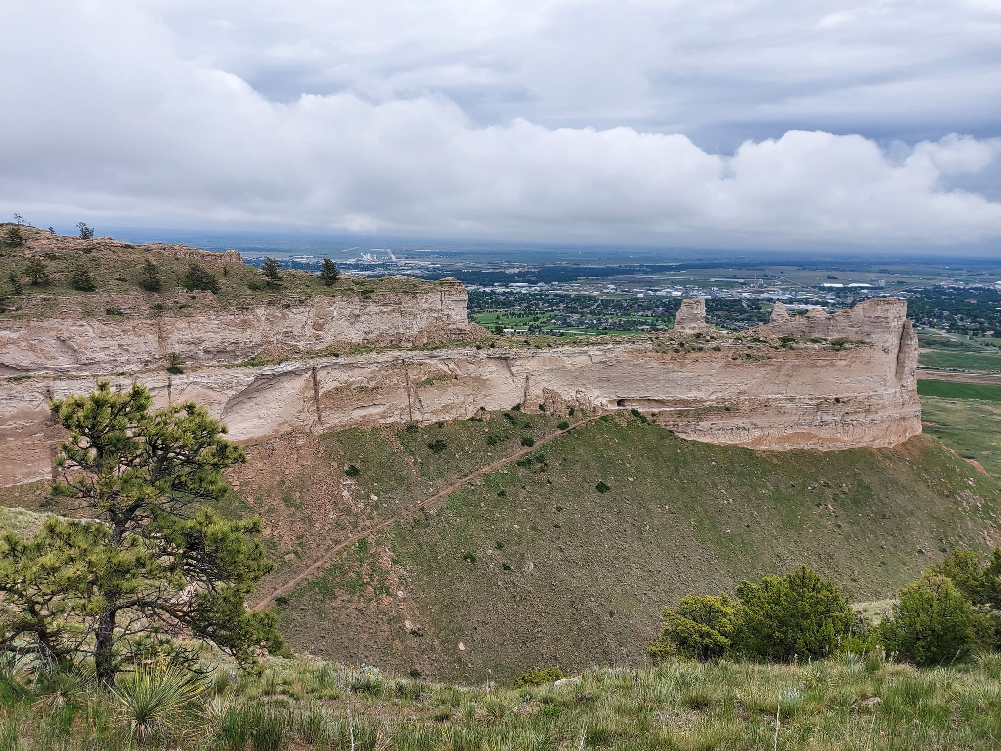 Panoramic view of rugged cliffs and green hills overlooking a distant town. - Saddle Rock Trail