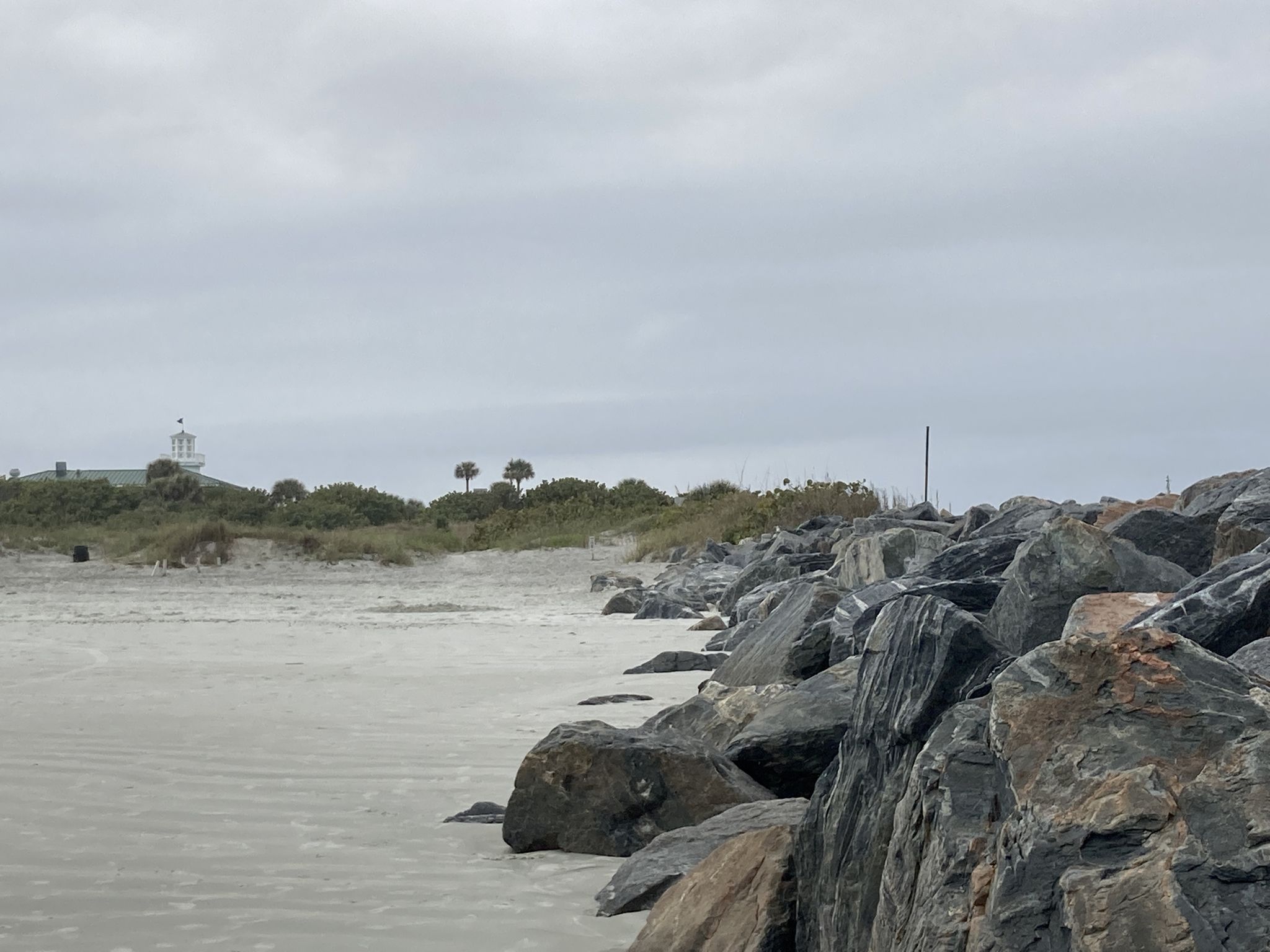 A rocky jetty borders a sandy beach under an overcast sky. - Hiking loop from Cape Canaveral