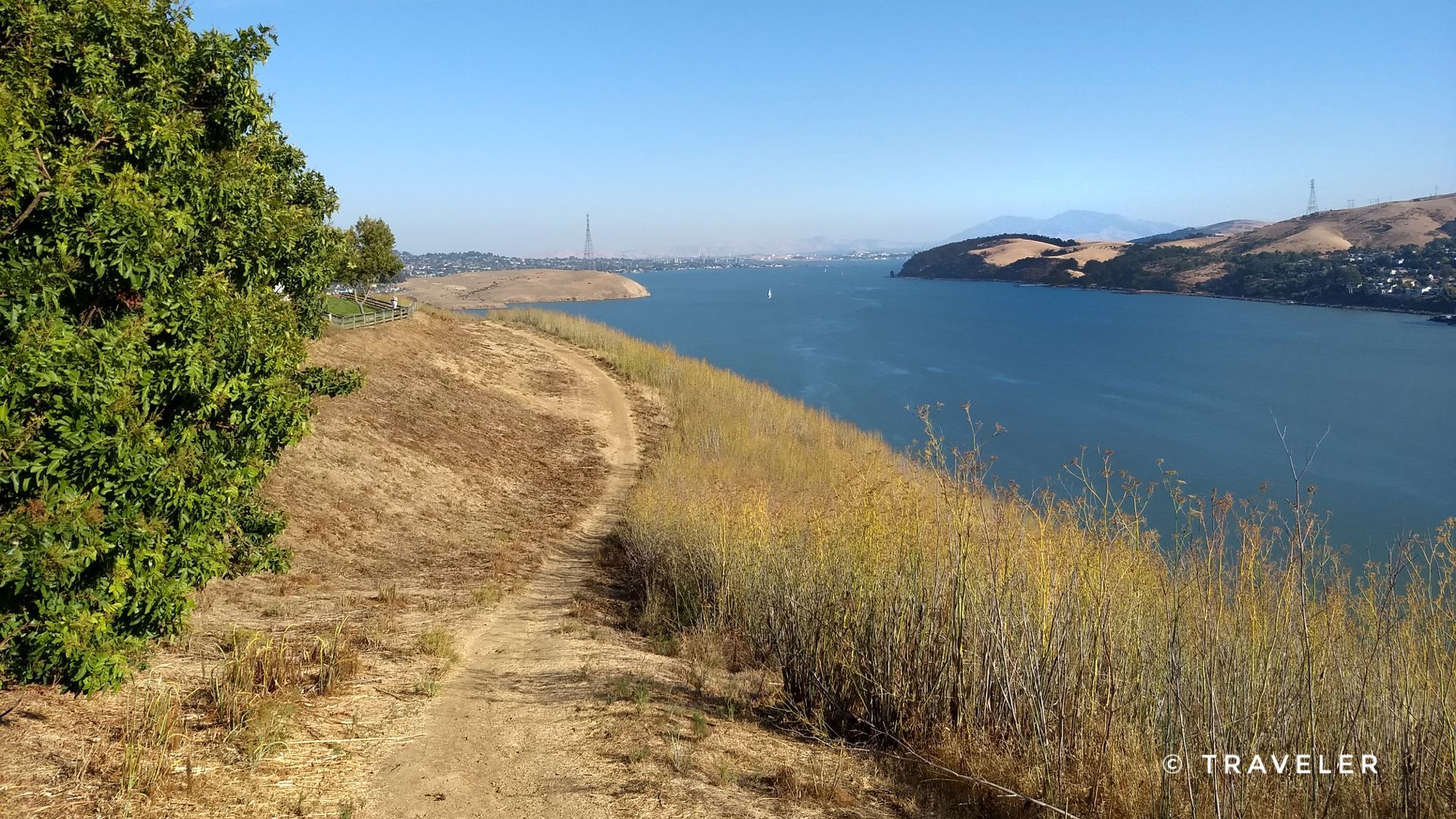 A dirt path winds along a dry grassy hillside overlooking a large body of water. - Lighthouse Vineyard – Carquinez Overlook Trail loop from Carquinez Bridge