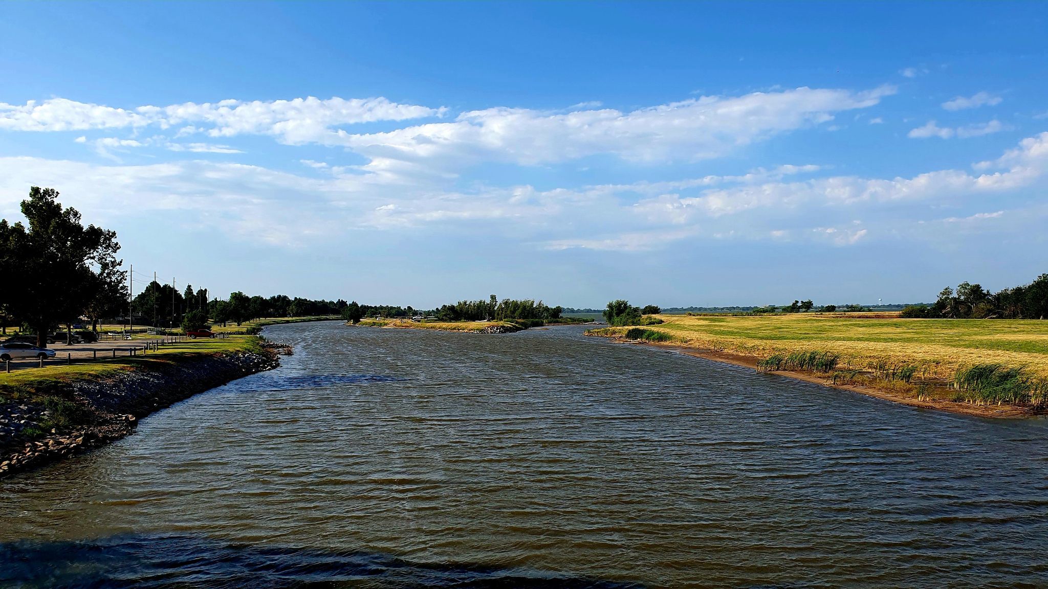 A wide river flows between green banks and distant trees under a blue sky. - Lake Overholser Bridge – Lake Overholser Dam loop from First Indian Pentecostal Church
