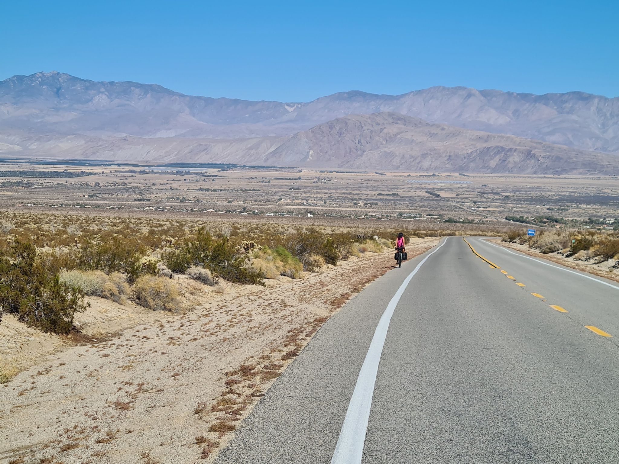 Cyclist on a long desert road with scrub brush and distant mountains. - Desert Eagle Sculpture – Yaqui Pass loop from Borrego Springs