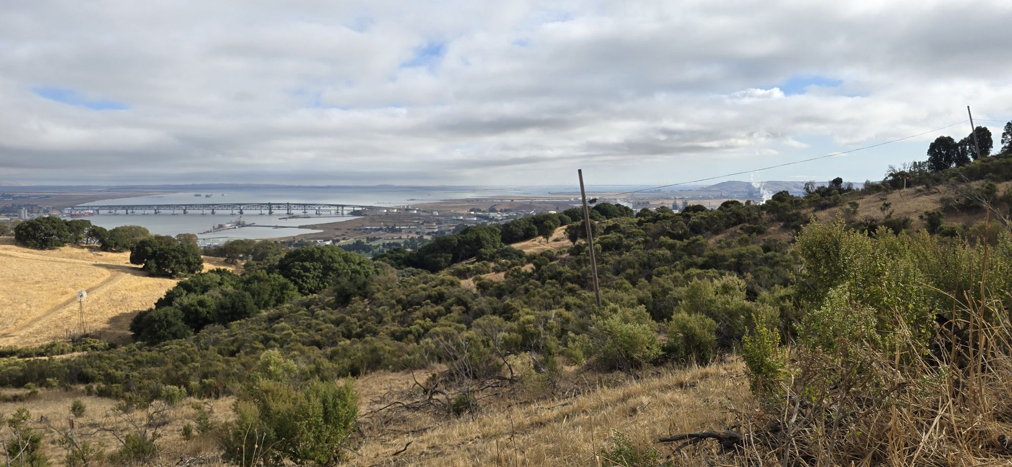 Overcast view of a distant bridge over water, surrounded by hills. - Aquatic Center loop from Martinez