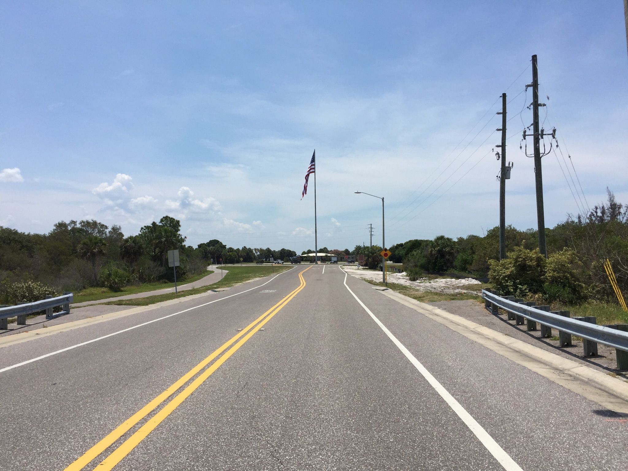 Paved road leading towards a large flag and distant buildings under a blue sky. - Fort De Soto Recreational Trail