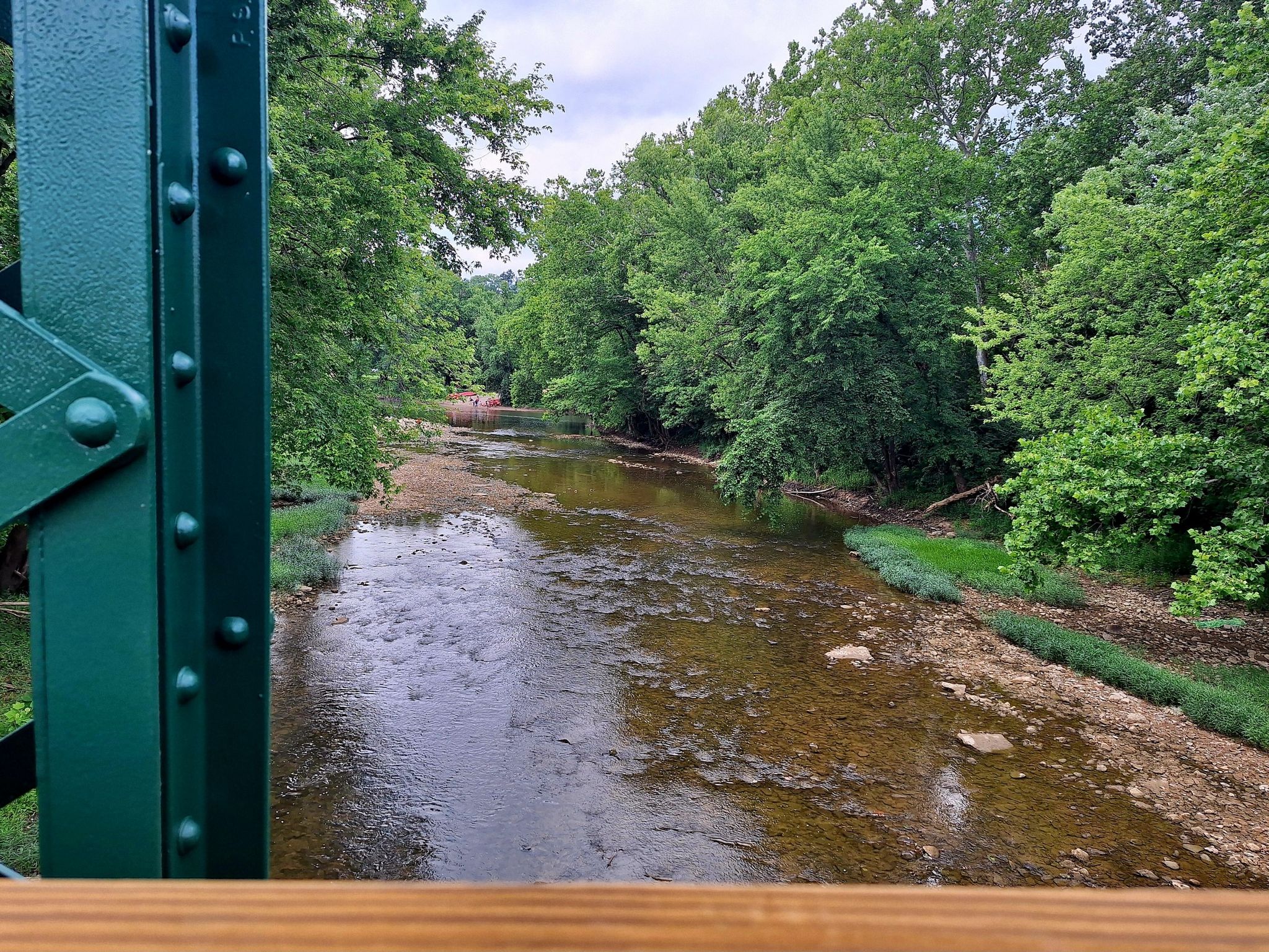 Green bridge structure overlooking a shallow river surrounded by lush trees. - Little Miami Scenic Trail
