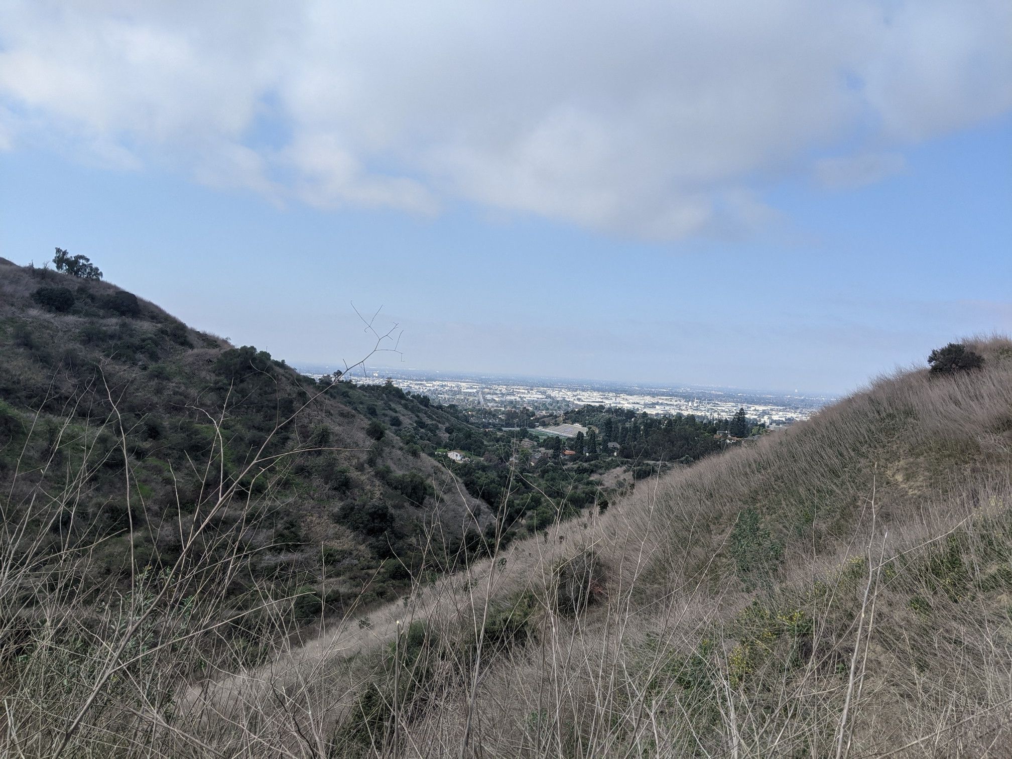 Dry hillsides frame a distant city under a bright, cloudy sky. - Workman Hill and Schabarum-Skyline Loop