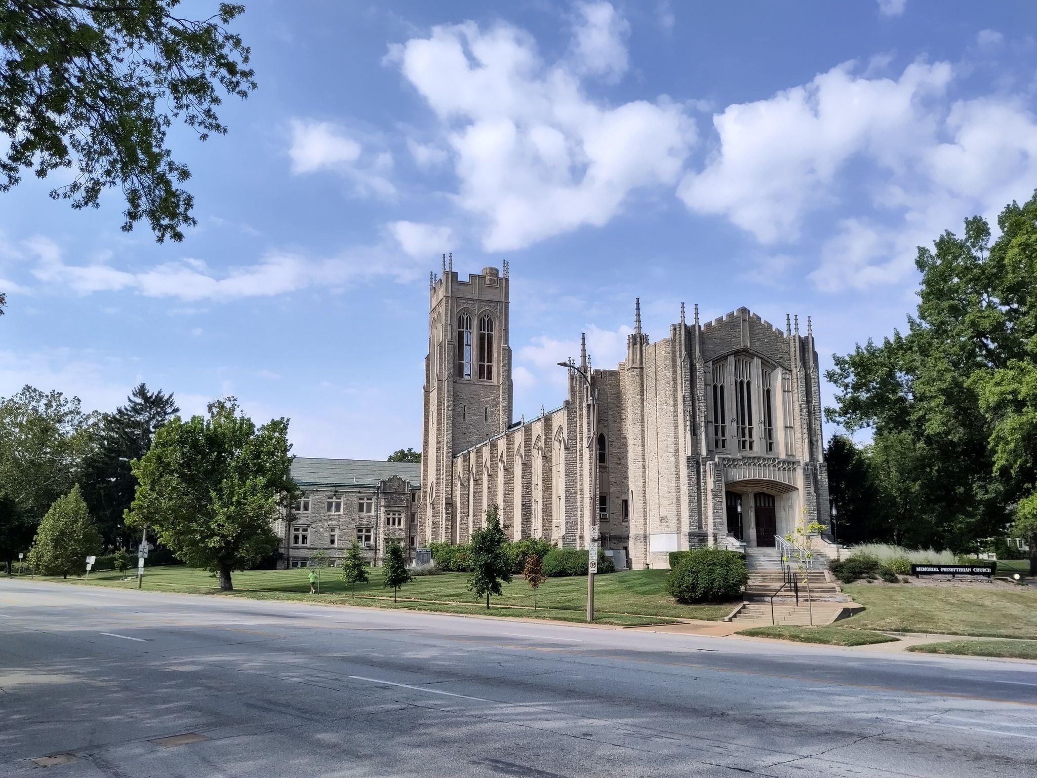 A grand stone building with a tall tower stands beside a road. - Wheels Path – Forest Park loop from Clayton