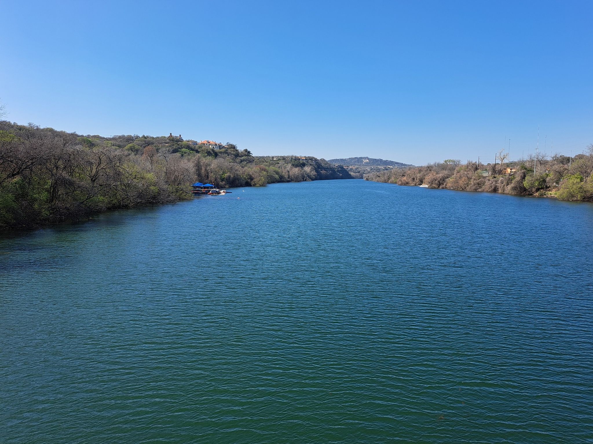 Wide river flowing between tree-lined banks under a clear blue sky. - Ann & Roy Butler Hike and Bike Trail