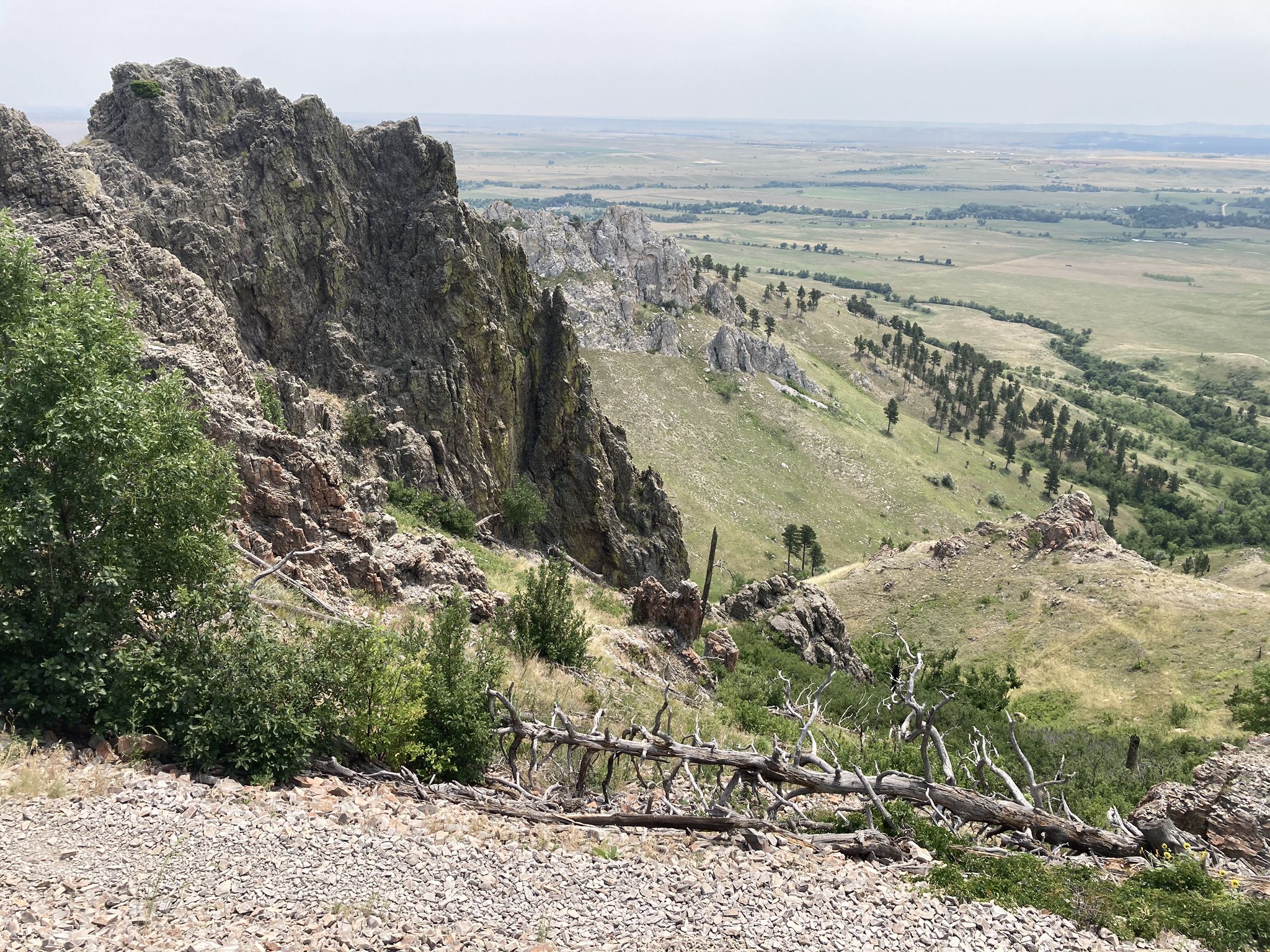 Rugged rocky cliffs and a steep hillside overlooking a vast, green plain. - Bear Butte