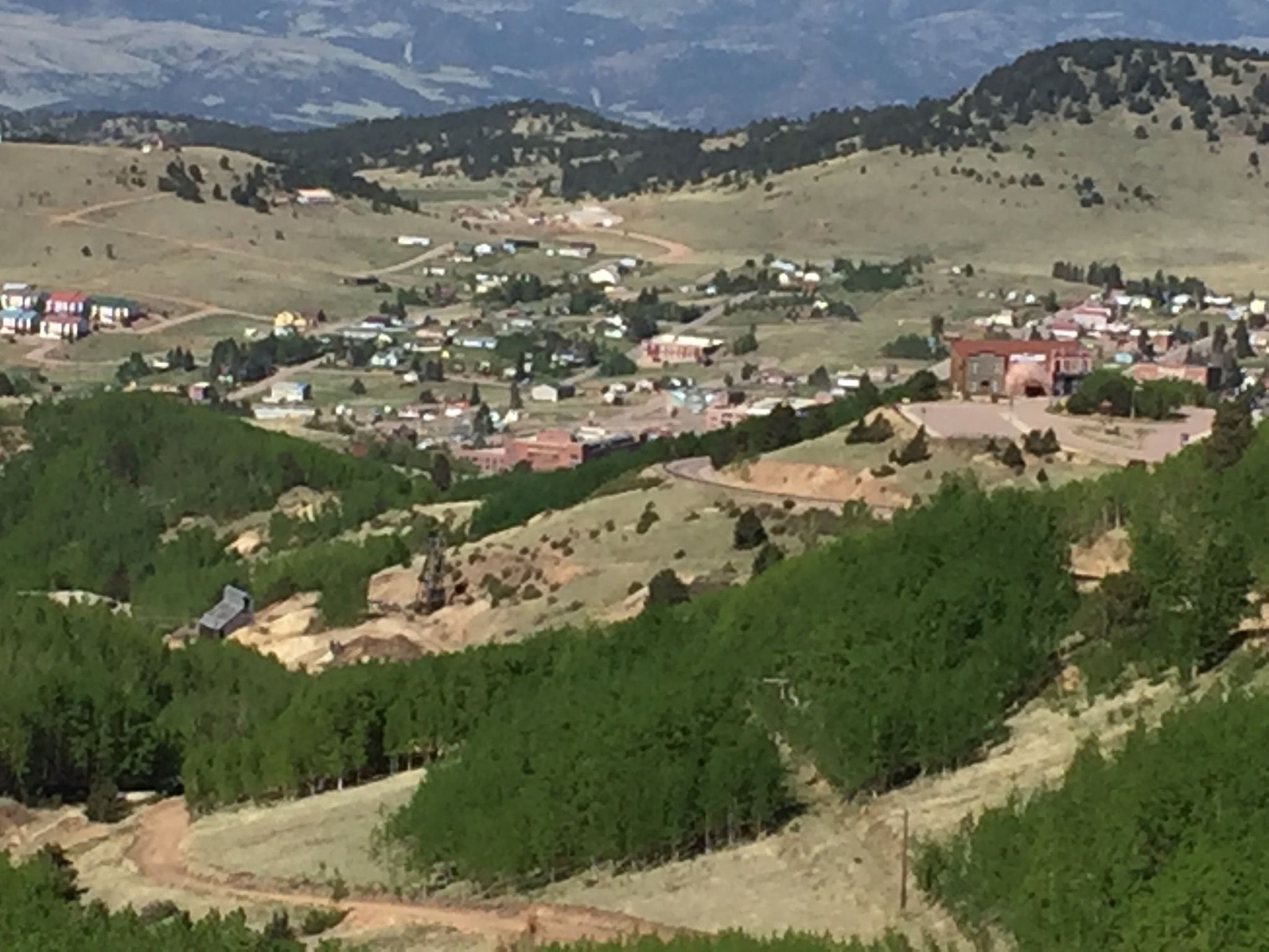 A small town built on a green hillside with scattered trees and distant mountains. - Mueller State Park from Cripple Creek