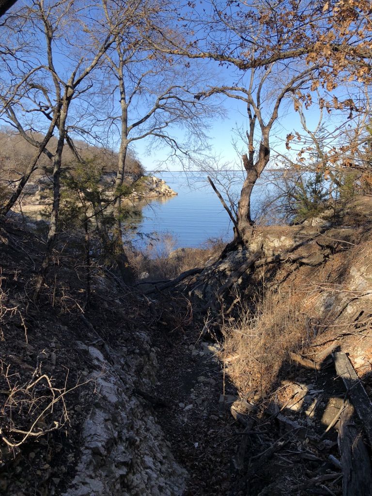 Rocky ravine with bare trees opens to a calm lake on a sunny day. - Buttonbush Scenic Point loop from Eisenhower State Park