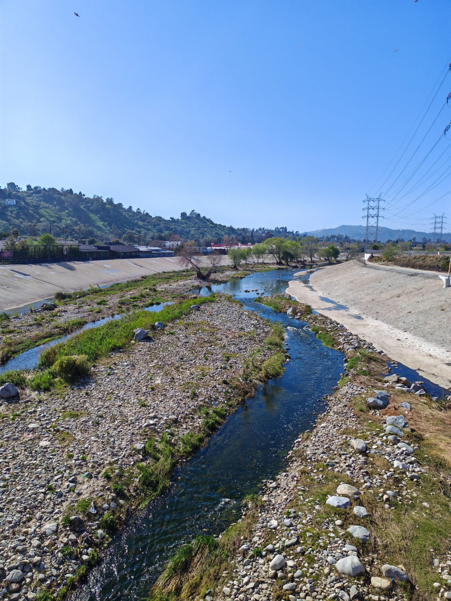 River flowing through a concrete channel with rocky banks and power lines. - Red Car Bridge – Sunnynook Pedestrian Bridge loop from Pershing Square
