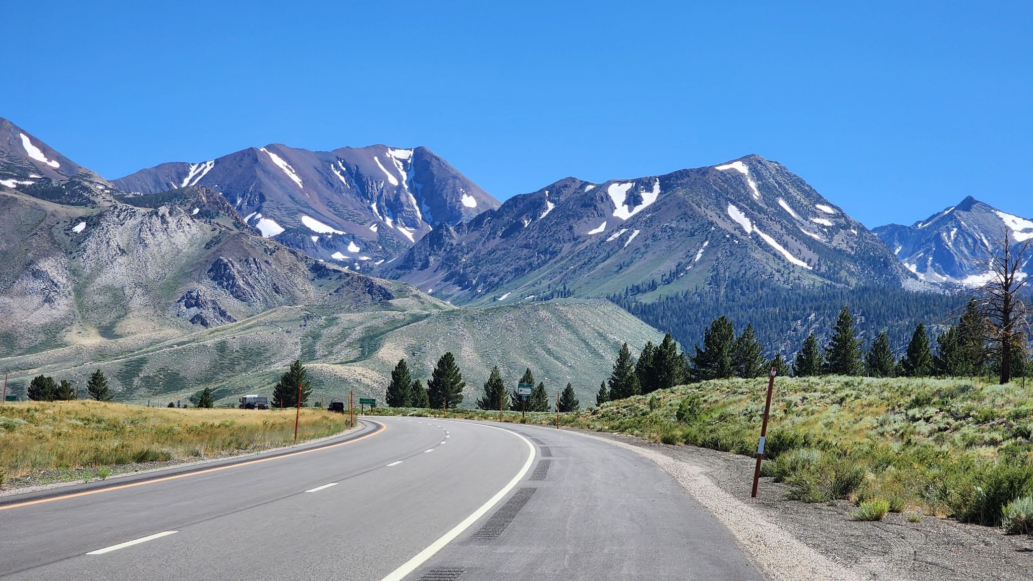 A winding road leads towards majestic, snow-capped mountains under a clear sky. - Mammoth Scenic Loop