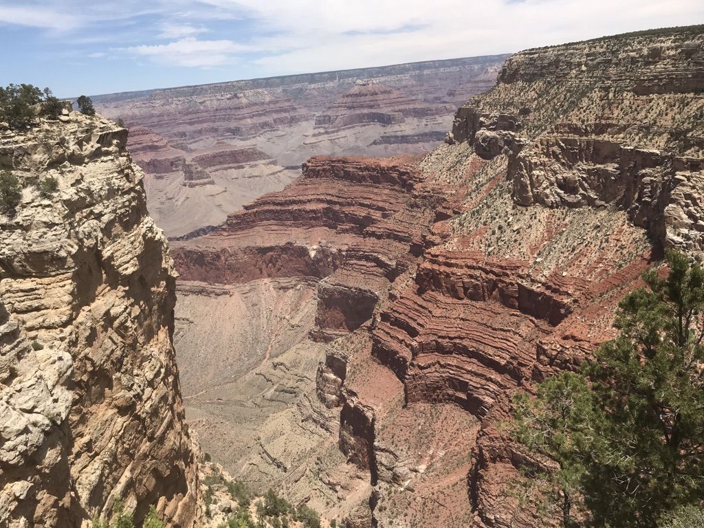 Wide canyon view with red and grey rock layers under a bright sky. - Grand Canyon Rim Trail